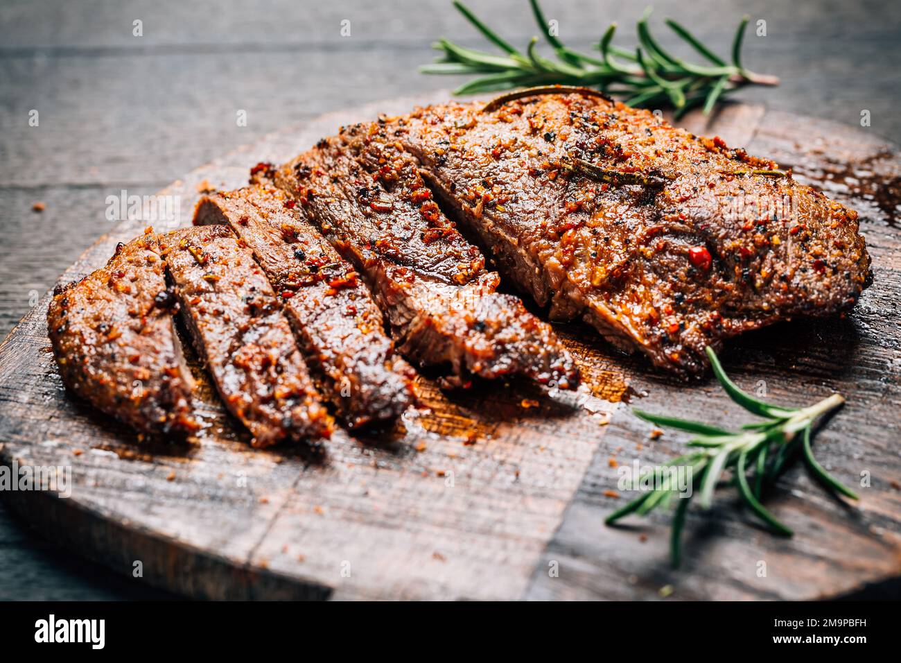 Steak de bœuf grillé avec épices sur planche à découper sur fond de bois Banque D'Images