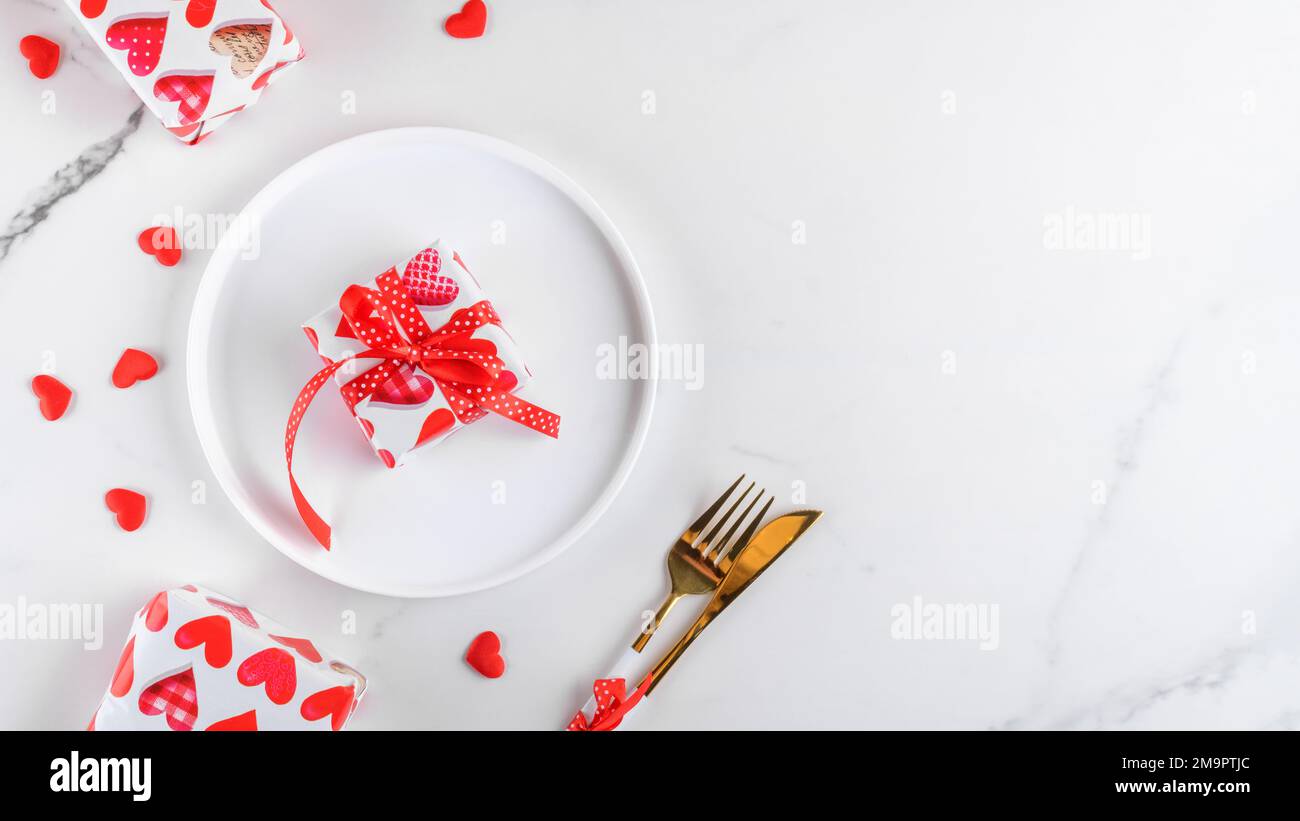 Dîner de Saint-Valentin avec cadeaux, coeurs rouges, fourchette et couteau sur marbre blanc. Décor romantique de table de vacances Banque D'Images