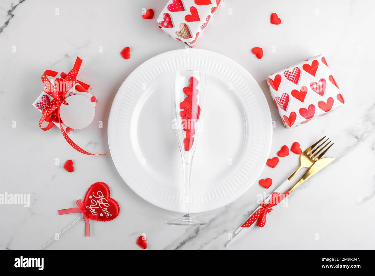 Dîner de Saint-Valentin avec cadeaux, verre de vin avec coeurs rouges, assiette, couverts sur fond de marbre blanc Banque D'Images