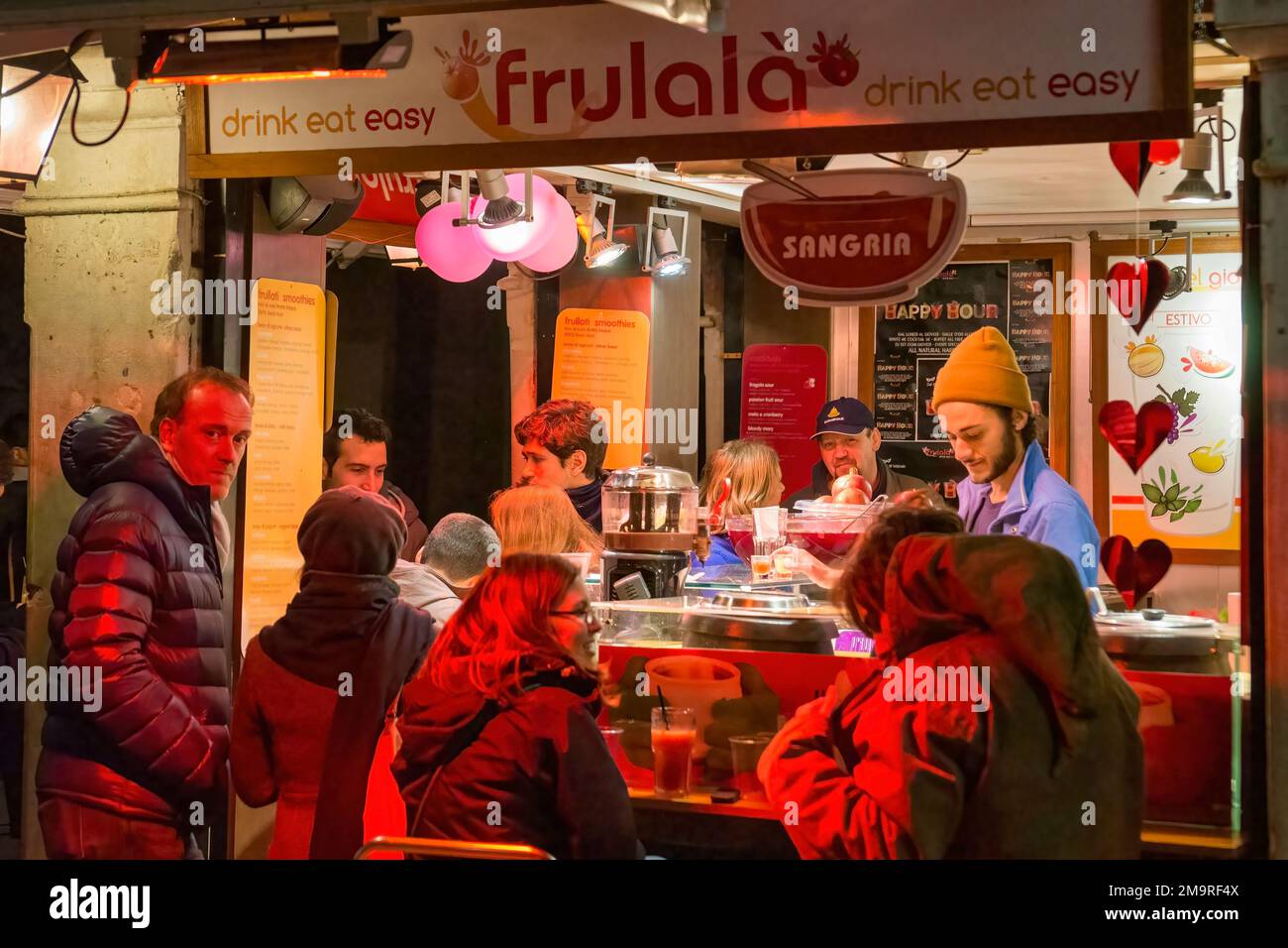 Les clients remplissent un bar de fruits de nuit dans une rue piétonne de Venise, Italie. Banque D'Images