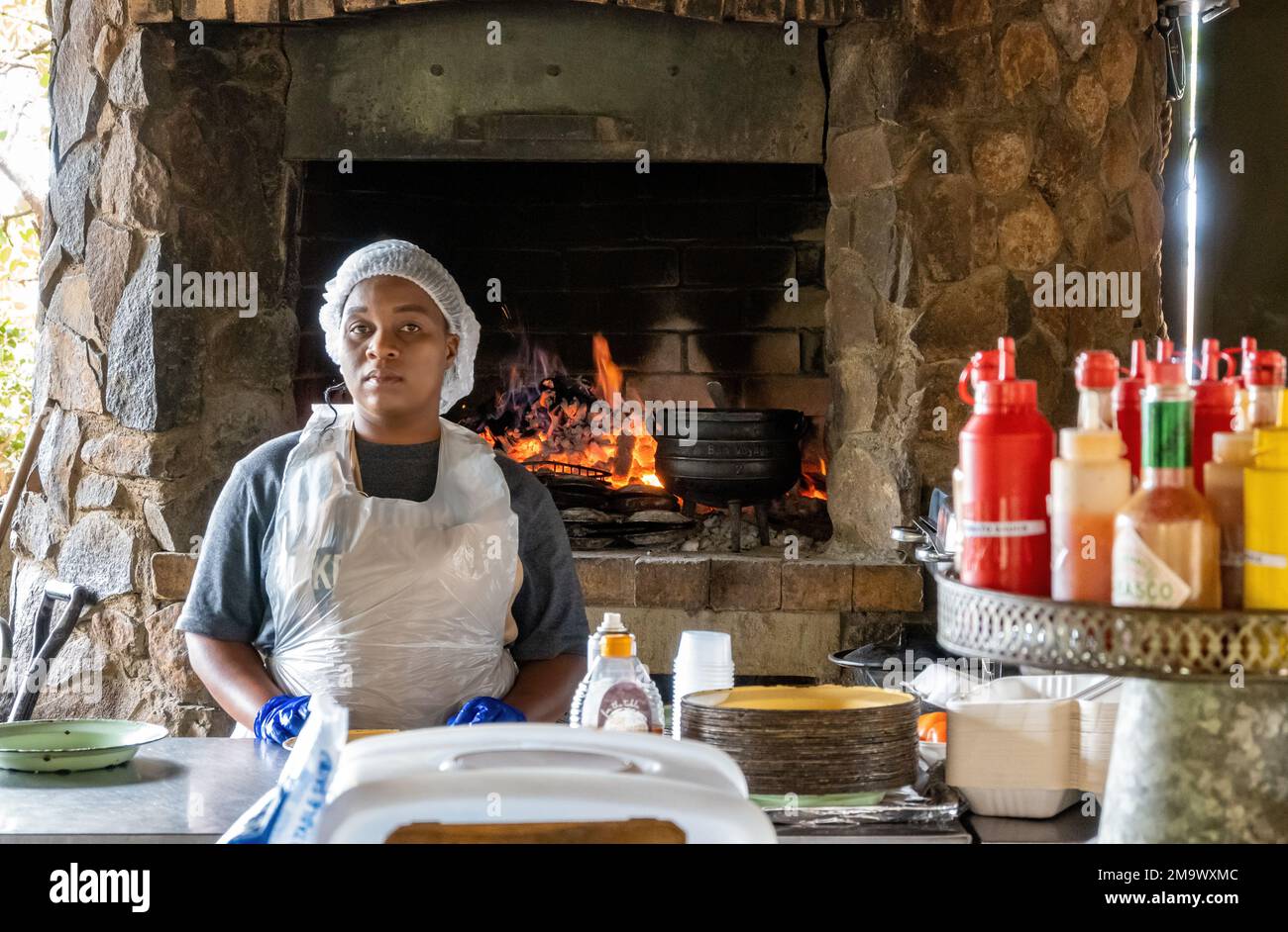 Une femme locale debout devant un poêle à feu dans un restaurant. Parc national Kruger, Afrique du Sud. Banque D'Images