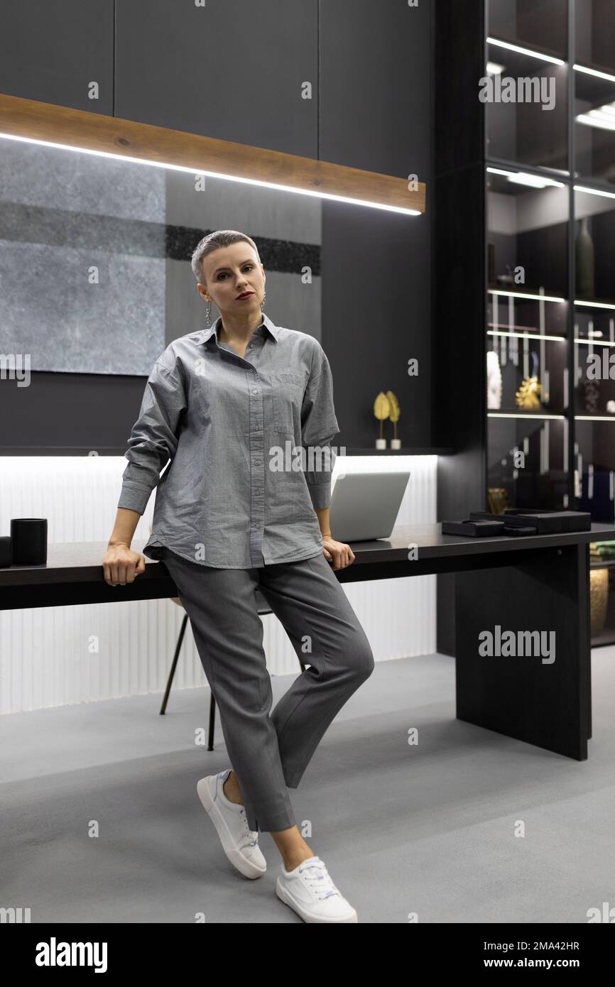 Une femme d'affaires avec une coupe courte dans une chemise grise dans un  bureau à la mode est enroulée sur le bord de la table Photo Stock - Alamy
