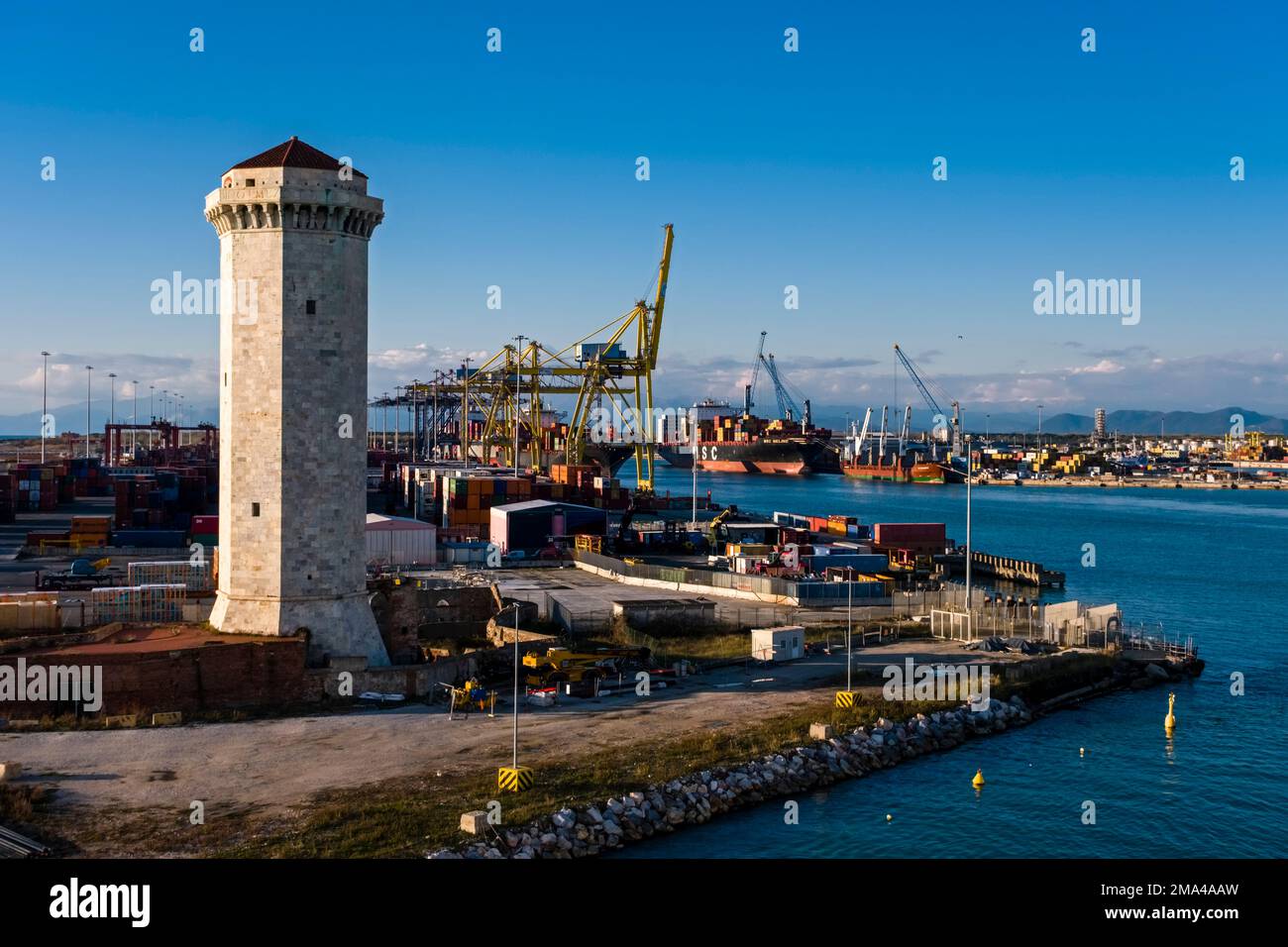 Phare, grues de déchargement des navires à conteneurs au port de Livourne, l'un des plus grands ports maritimes de la mer Méditerranée, au loin. Banque D'Images