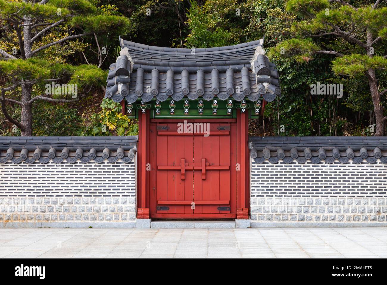 Portail en bois rouge sous toit carrelé. Architecture orientale traditionnelle dans le parc public de Busan, Corée du Sud Banque D'Images