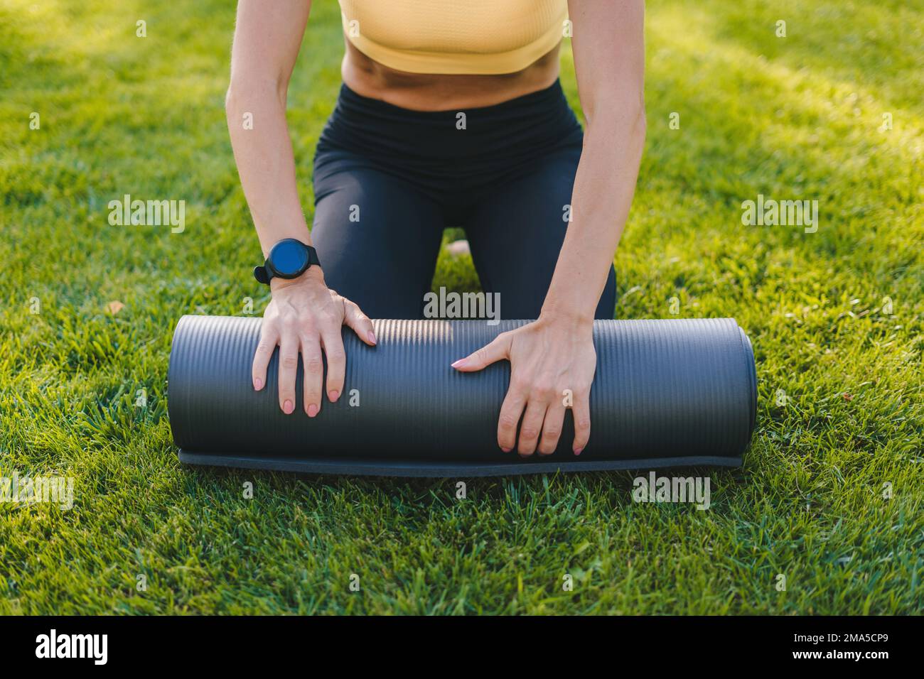 Gros plan des mains de la femme roulant son tapis de yoga après une séance  d'entraînement dans le jardin avec de l'herbe verte. Relaxation pratiquer  la méditation de yoga en plein air,