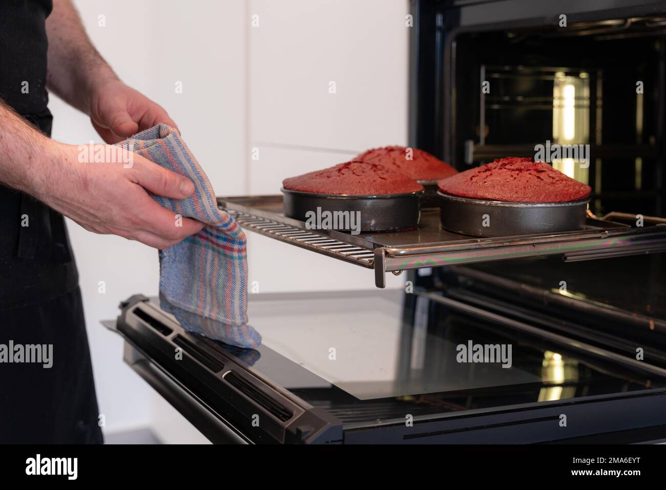 Un boulanger d'homme cuit un gâteau de velours rouge à la maison, en prenant le gâteau cuit hors des casseroles du four Banque D'Images