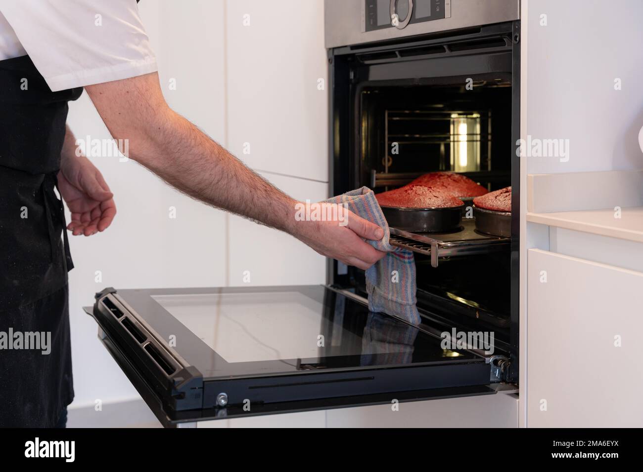 Un boulanger d'homme cuit un gâteau de velours rouge à la maison, en  préparant le gâteau en ajoutant de l'huile dans le robot de cuisine, le  travail à la maison Photo Stock -