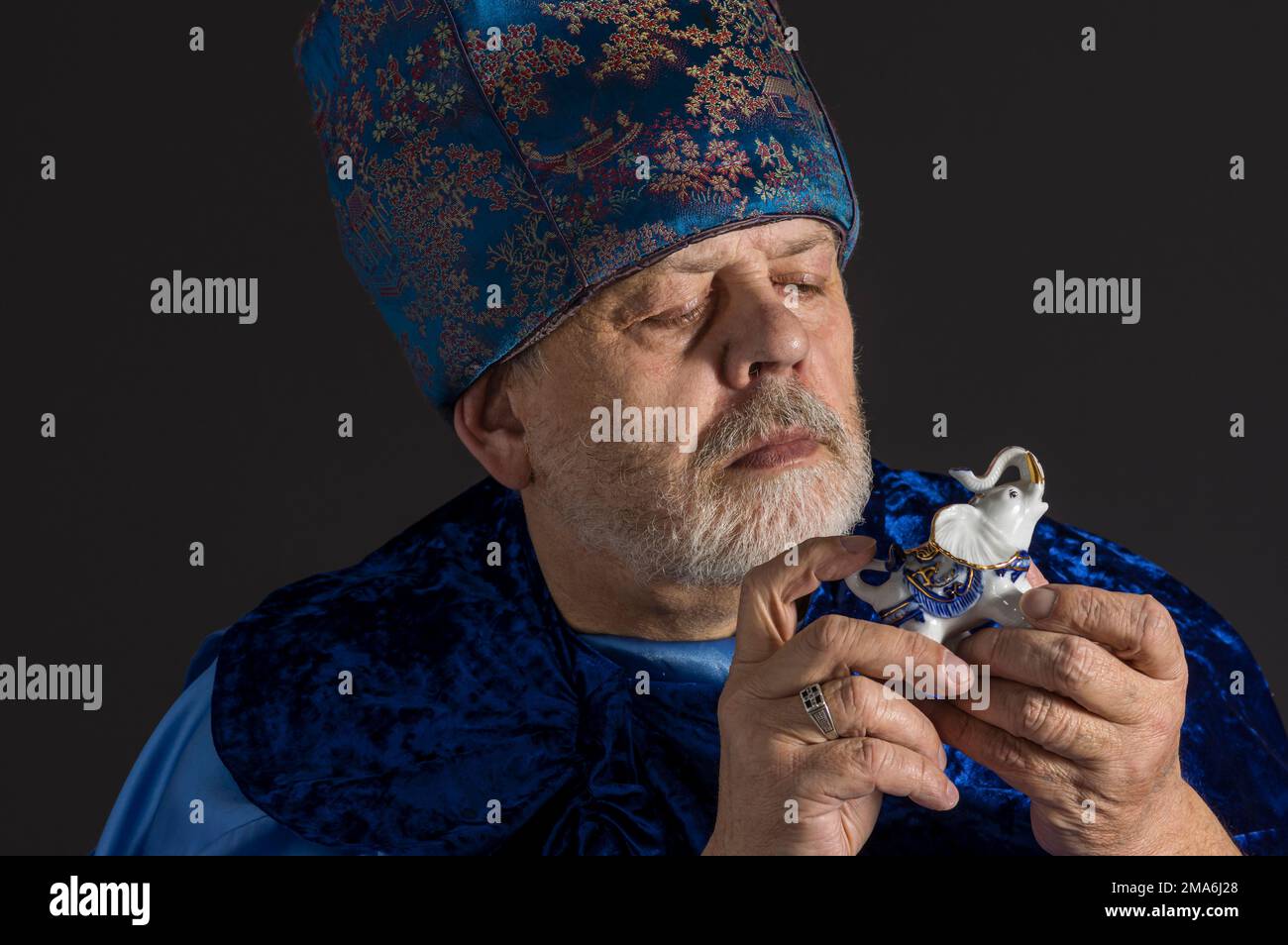 Joli portrait de l'homme âgé barbu en vêtements orientaux bleus prenant la figure en porcelaine d'éléphant et la voir Banque D'Images