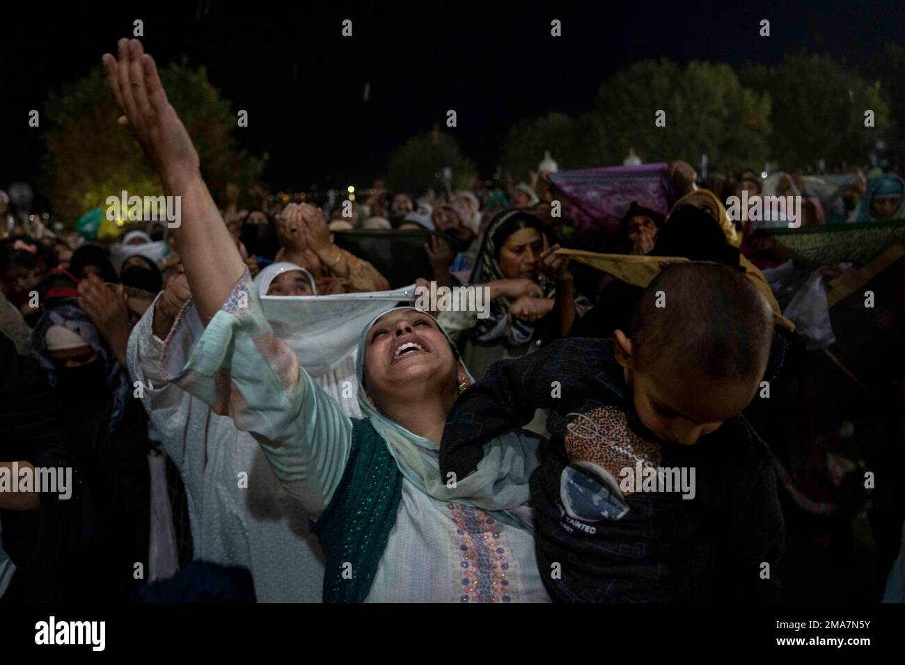A Kashmiri Muslim woman holds a child while praying, as a head priest ...