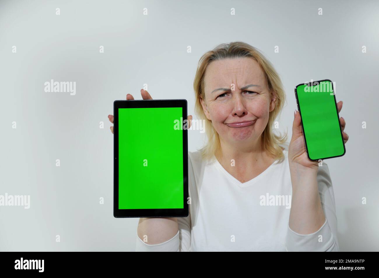 femme frowned tenant tablette et téléphone montre vert chroma clé écran elle est blanc vêtements place pour le texte de la publicité en ligne formation émotions désagréables surprise facture d'augmentation de prix Banque D'Images