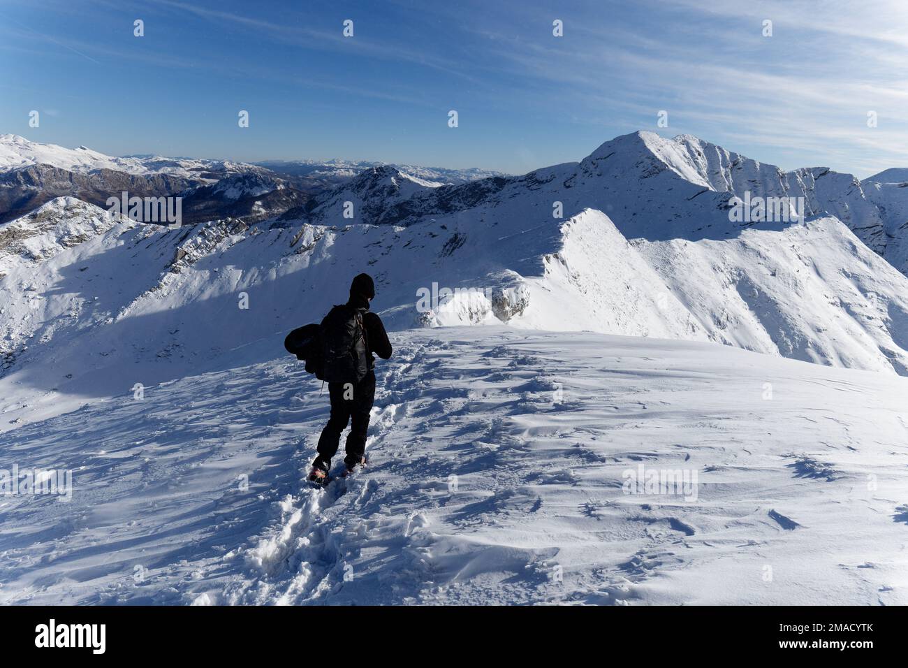 Randonnée solo en direction du sommet de la montagne avec une crête de montagne difficile entre les deux. Vaste paysage de montagne d'hiver plein de neige. Randonnée en hiver. Banque D'Images