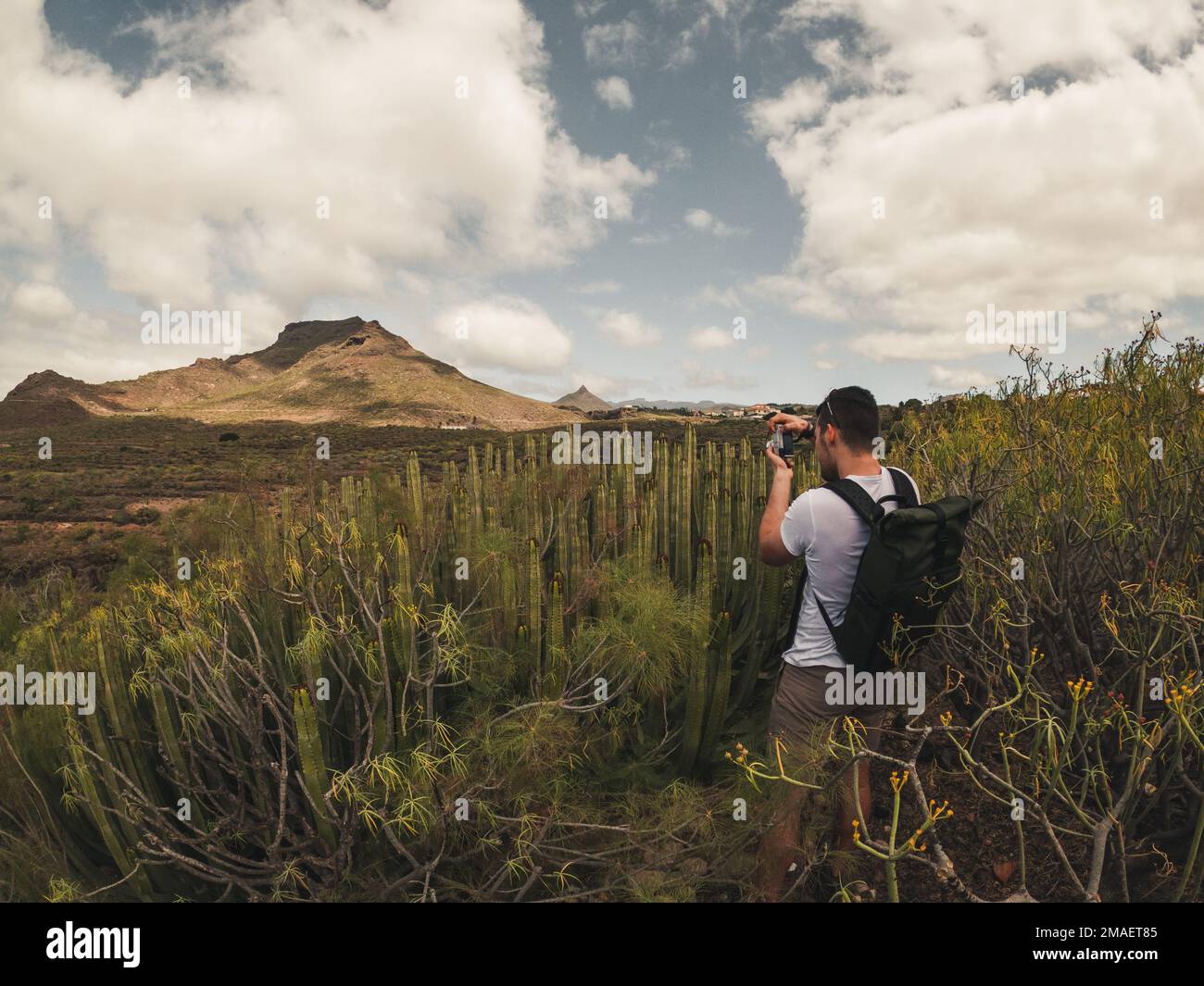 Jeune homme caucasien avec des cheveux foncés et des sacs de photographie de paysage avec des cactus et des montagnes à Arona, Ténérife. Banque D'Images