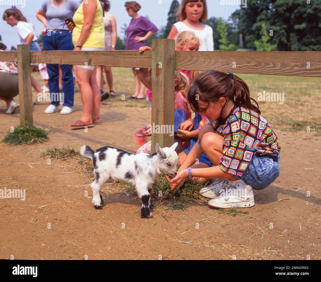 Les enfants qui allaitent leur bébé de chèvre dans la ferme pour enfants, Cotswold Wildlife Park & Gardens, Burford, Oxfordshire, Angleterre, Royaume-Uni Banque D'Images