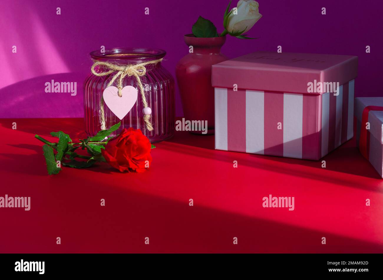 La Saint-Valentin. Rose rouge dans un vase en verre sur fond rose. Banque D'Images