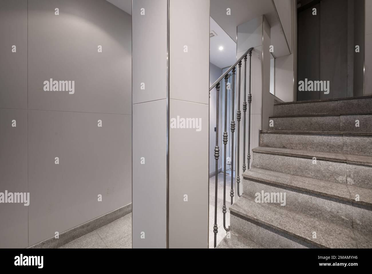 Portail avec carreaux de granit sur les escaliers pour accéder à un ascenseur avec portes grises et rambarde en fer forgé Banque D'Images