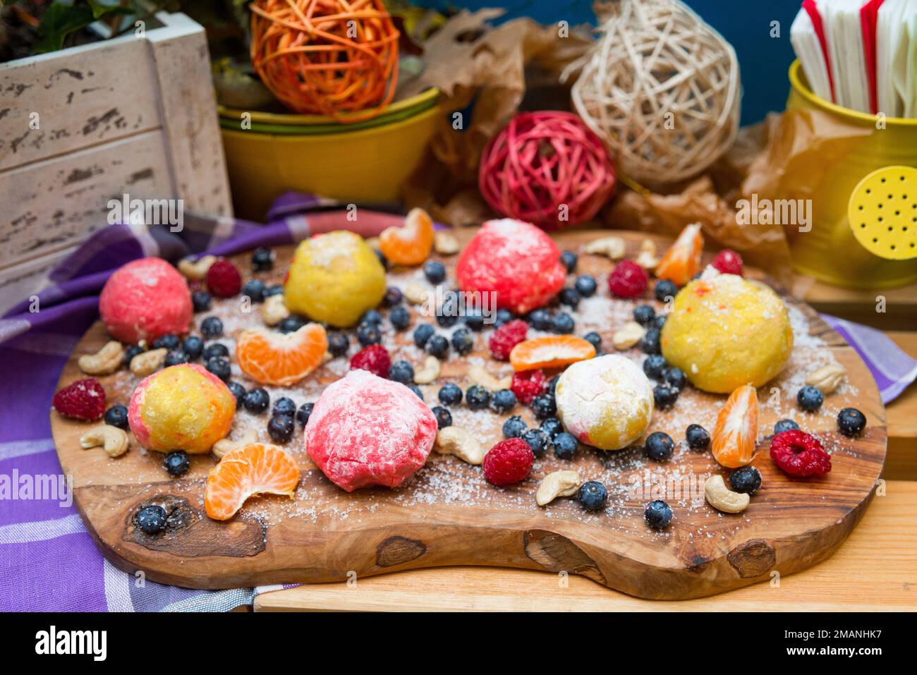 Boulettes de massepain en sucre sur une planche avec des bleuets et des framboises frais, des tranches de mandarine et des noix de cajou Banque D'Images