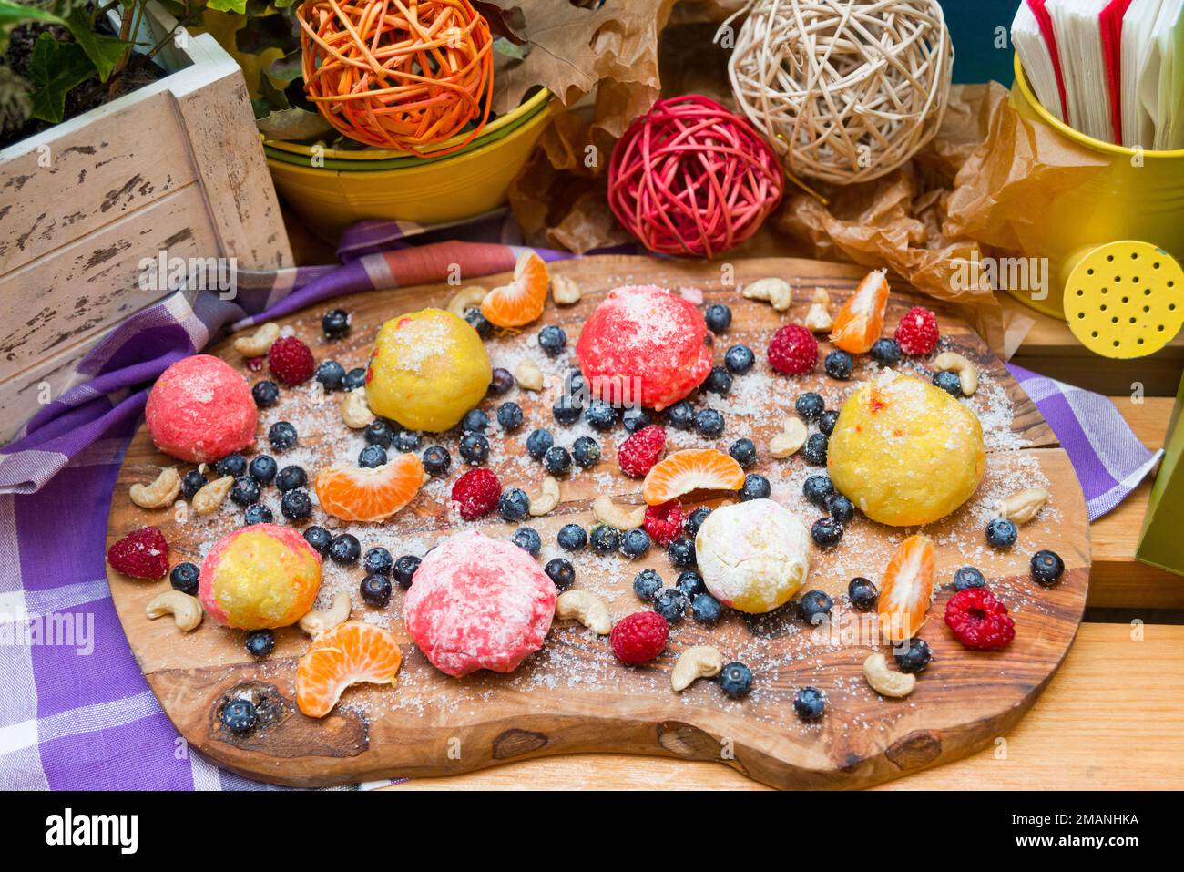 Boulettes de massepain en sucre sur une planche avec des bleuets et des framboises frais, des tranches de mandarine et des noix de cajou Banque D'Images