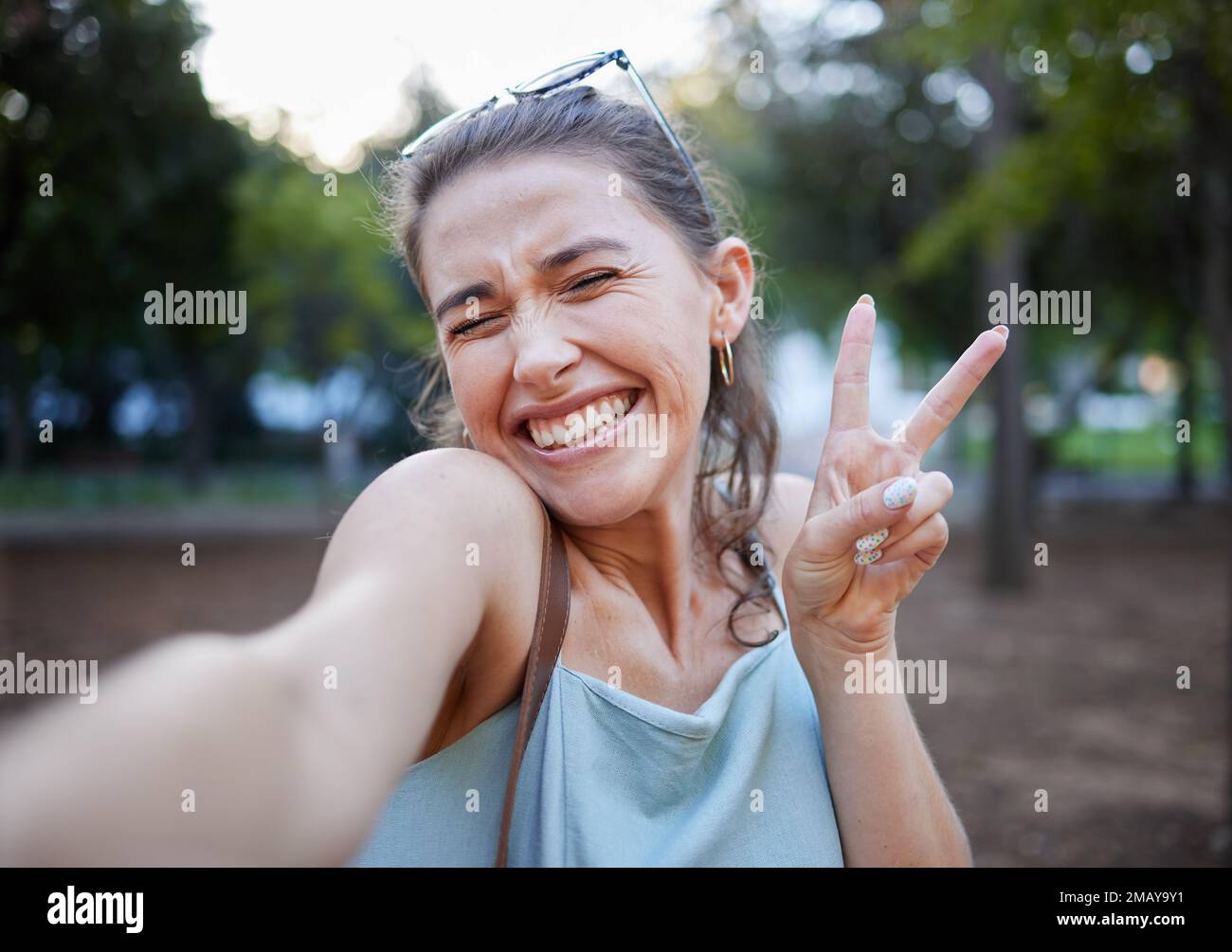 Selfie, paix et visage avec une femme dans un parc, posant pour une photo seule en plein air dans la nature. Les médias sociaux, emoji et le signe de main avec un attrayant Banque D'Images