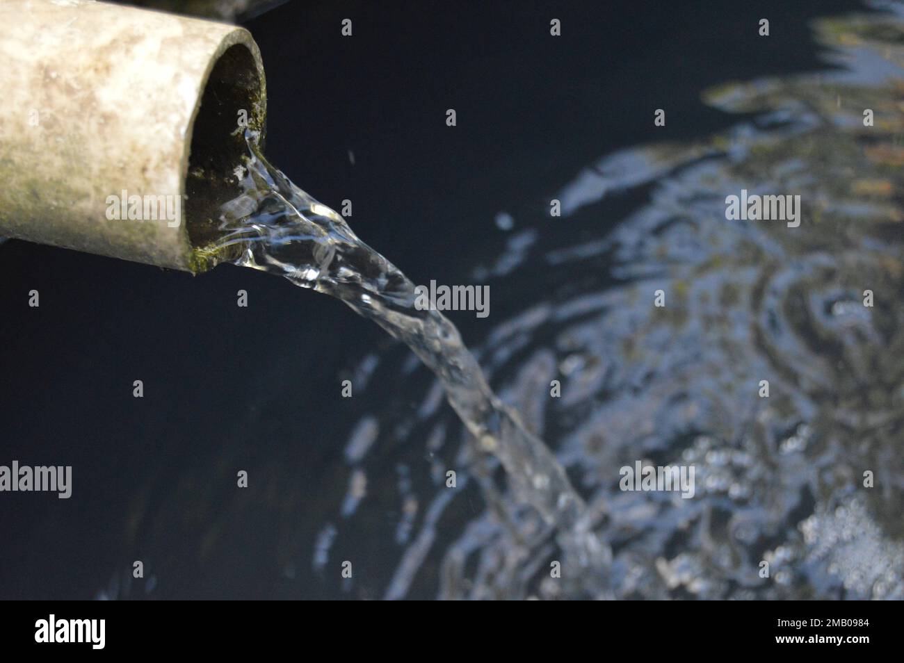 Portrait de l'eau déversée par un tuyau de vidange dans un fossé noir. Banque D'Images