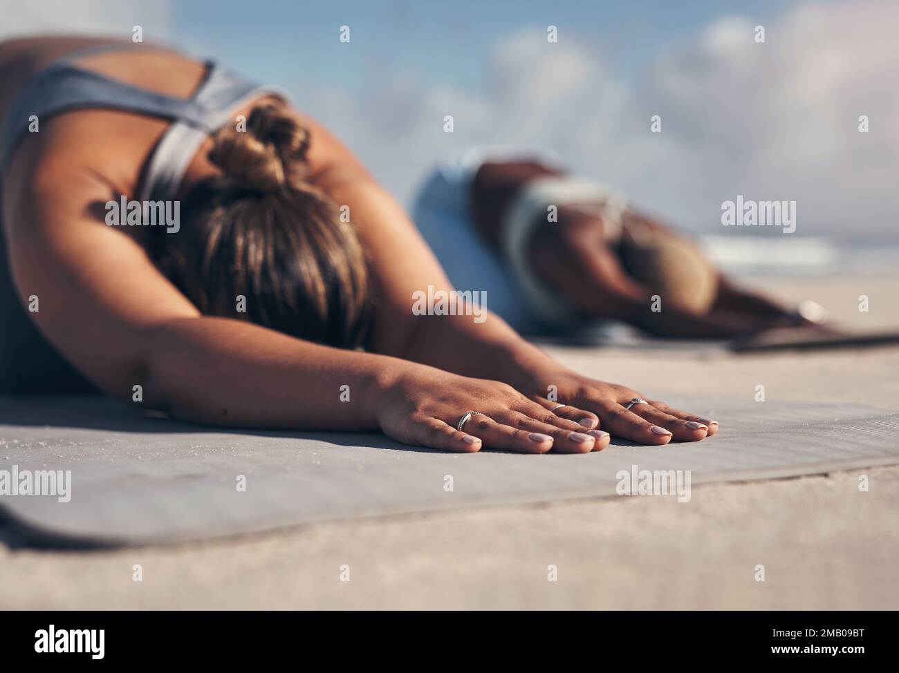 Le yoga vous aide à Ralentis. deux jeunes femmes pratiquant le yoga sur la plage. Banque D'Images