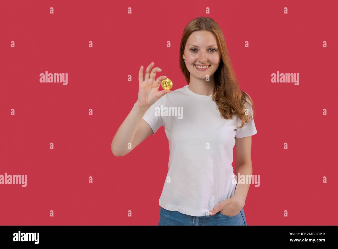 Jeune femme d'affaires souriante dans une chemise blanche tenant le bitcoin à la main posant isolée sur fond de mur rose. Concept d'entreprise de patrimoine de carrière. Placez-le sur une copie de l'emplacement. Banque D'Images