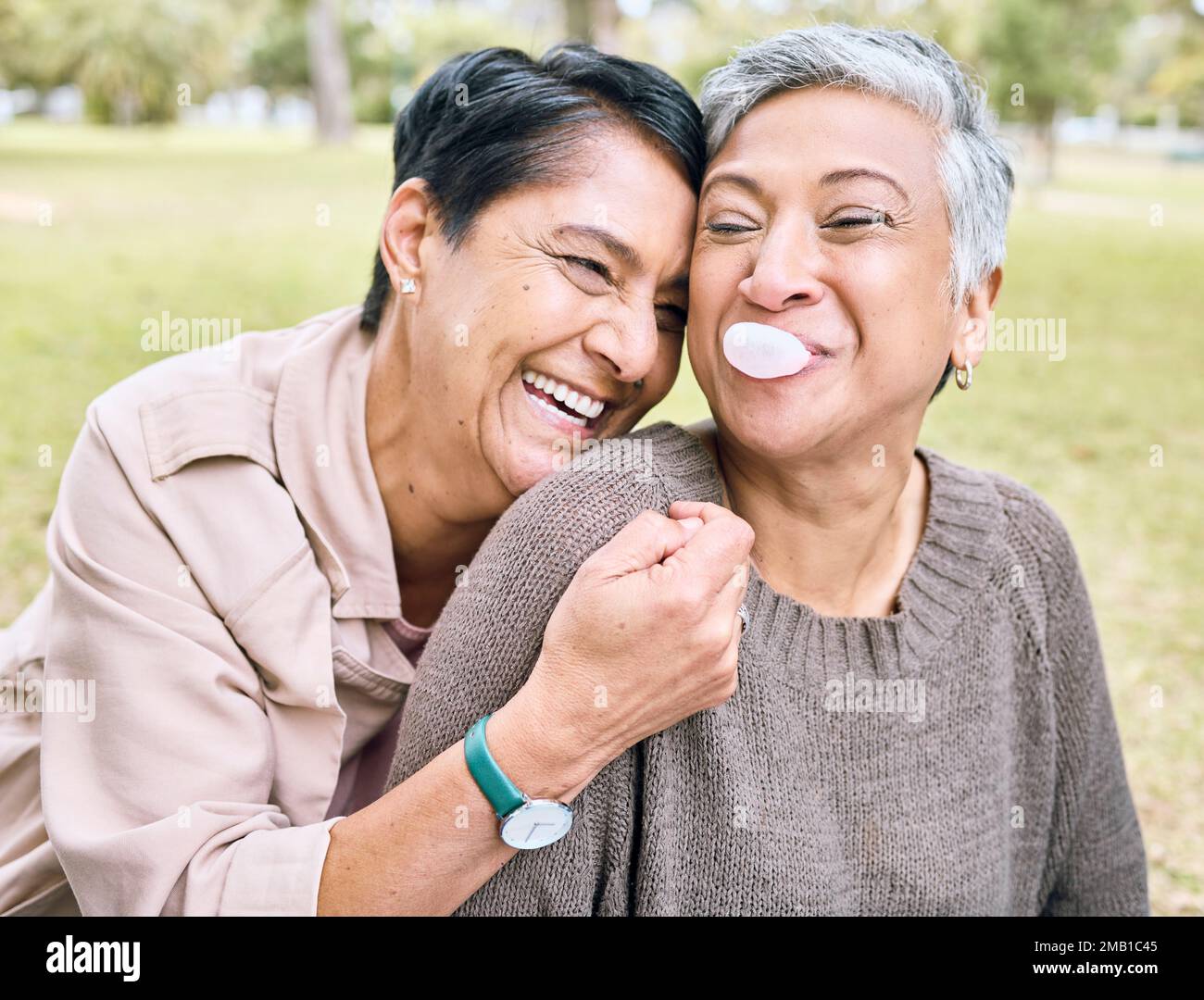 Des femmes âgées, des amis et des hugs dans le parc pour des comiques, drôle et heureux temps ensemble dans la nature avec bubblegum. Vieille femme, étreinte et riant pour la mémoire Banque D'Images