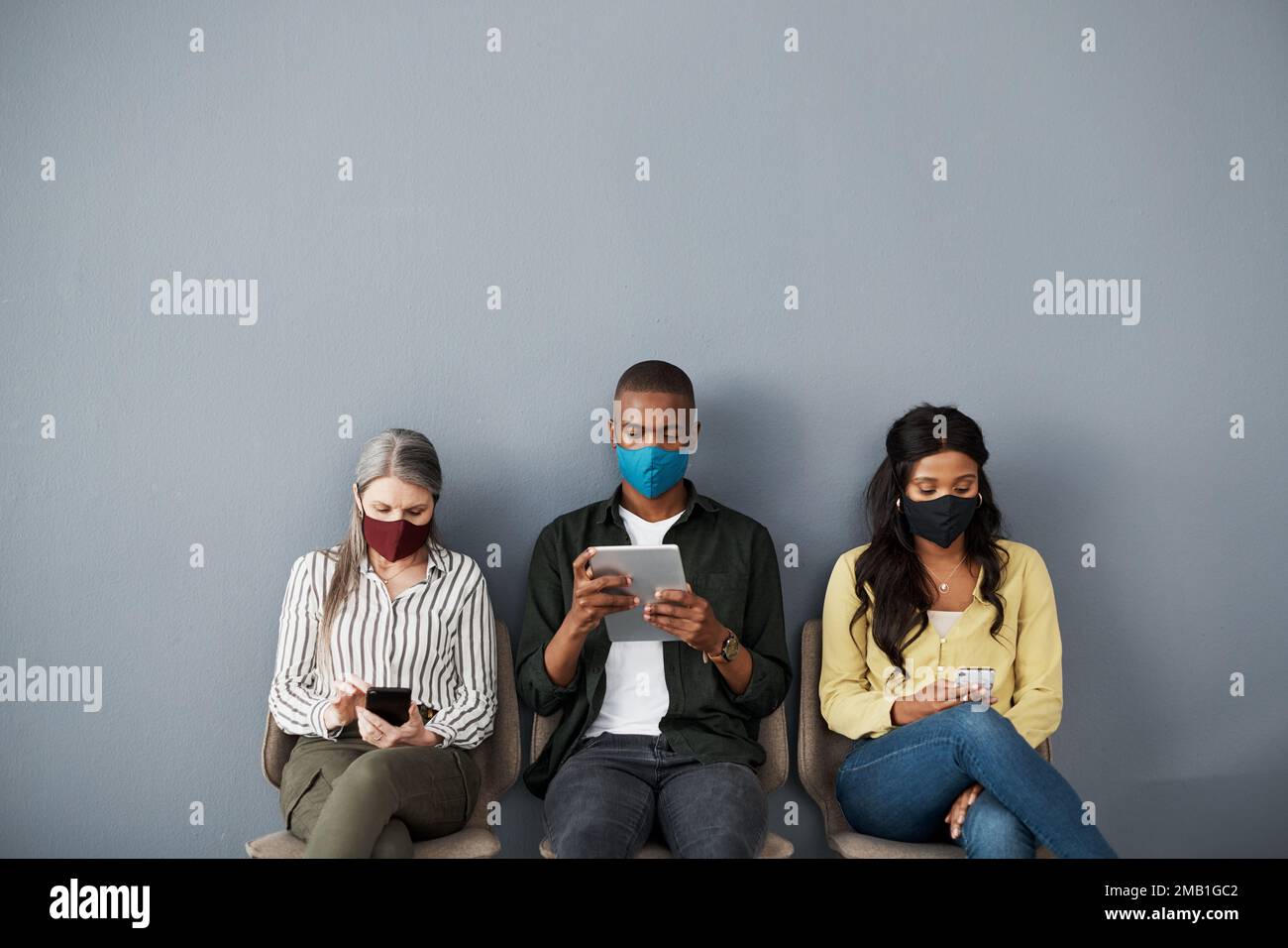 Allez jusqu'à ça comme si rien ne lui est plus. un groupe prudent de personnes qui prennent des distances socialement tout en utilisant leurs appareils intelligents contre un mur gris. Banque D'Images