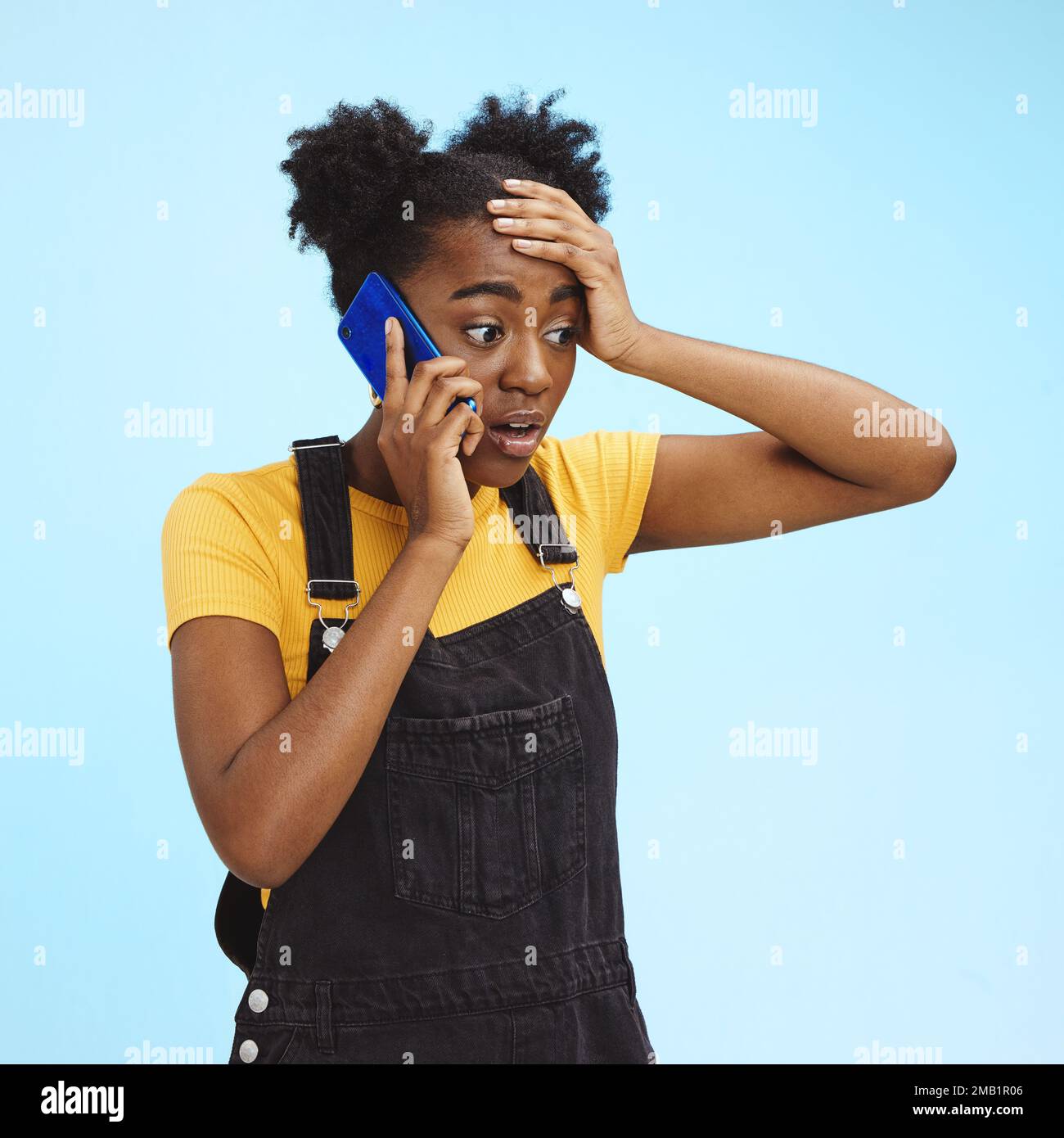 Femme noire, surprise et choquée lors d'un appel téléphonique pour des nouvelles isolée sur un fond bleu en studio. Wow, folle et africaine fille parlant de potins Banque D'Images