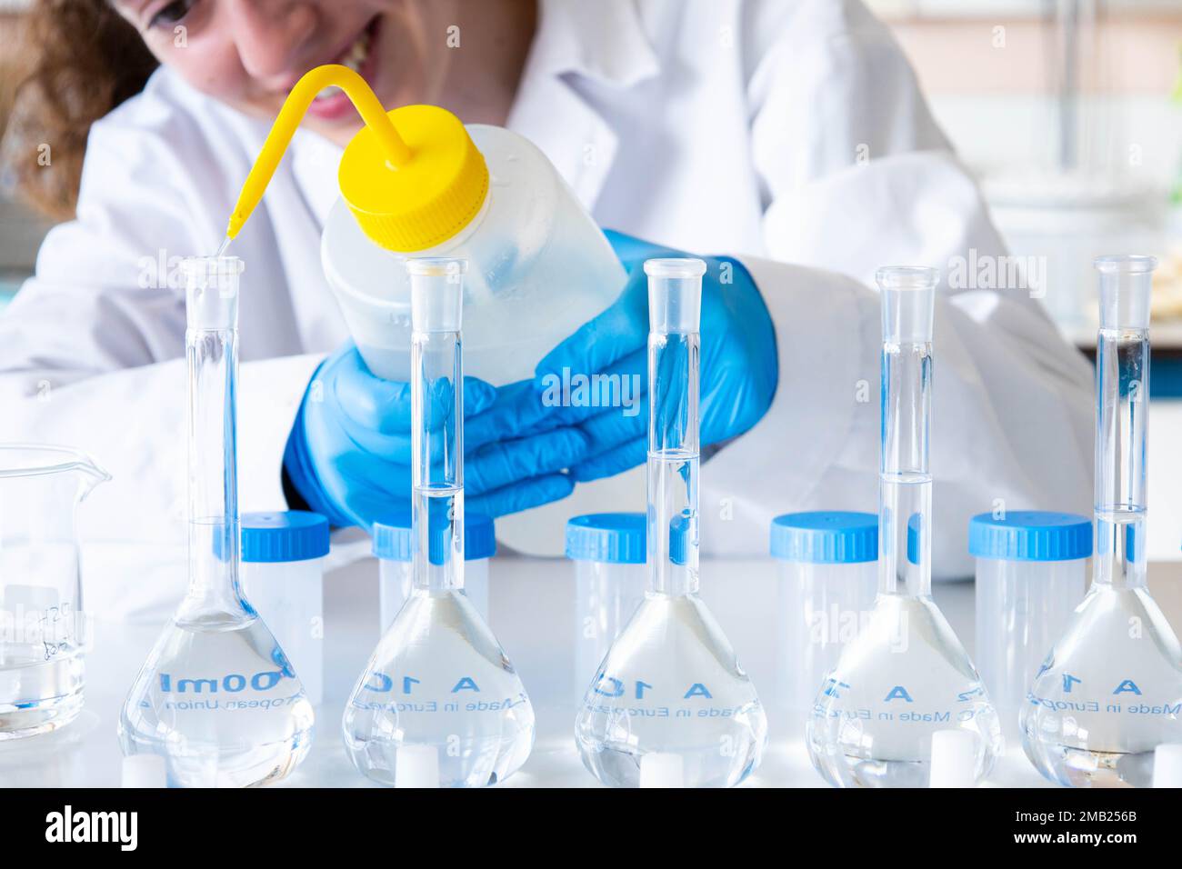 Gros plan scientifique femme nivelant une fiole jaugée avec un compte-gouttes portant des gants et de l'équipement bleus. Bonne fille de technicien de laboratoire travaillant. Banque D'Images