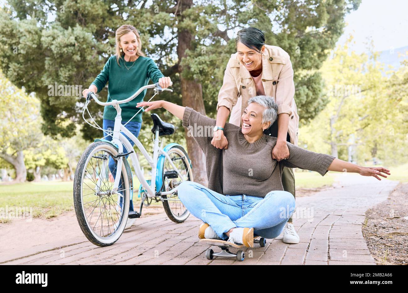 Comique, heureux et amis de retraite dans le parc pour le plaisir de plein air stupide avec le skateboard et la bicyclette. Drôle, goofy et les femmes âgées dans la nature avec excitée Banque D'Images