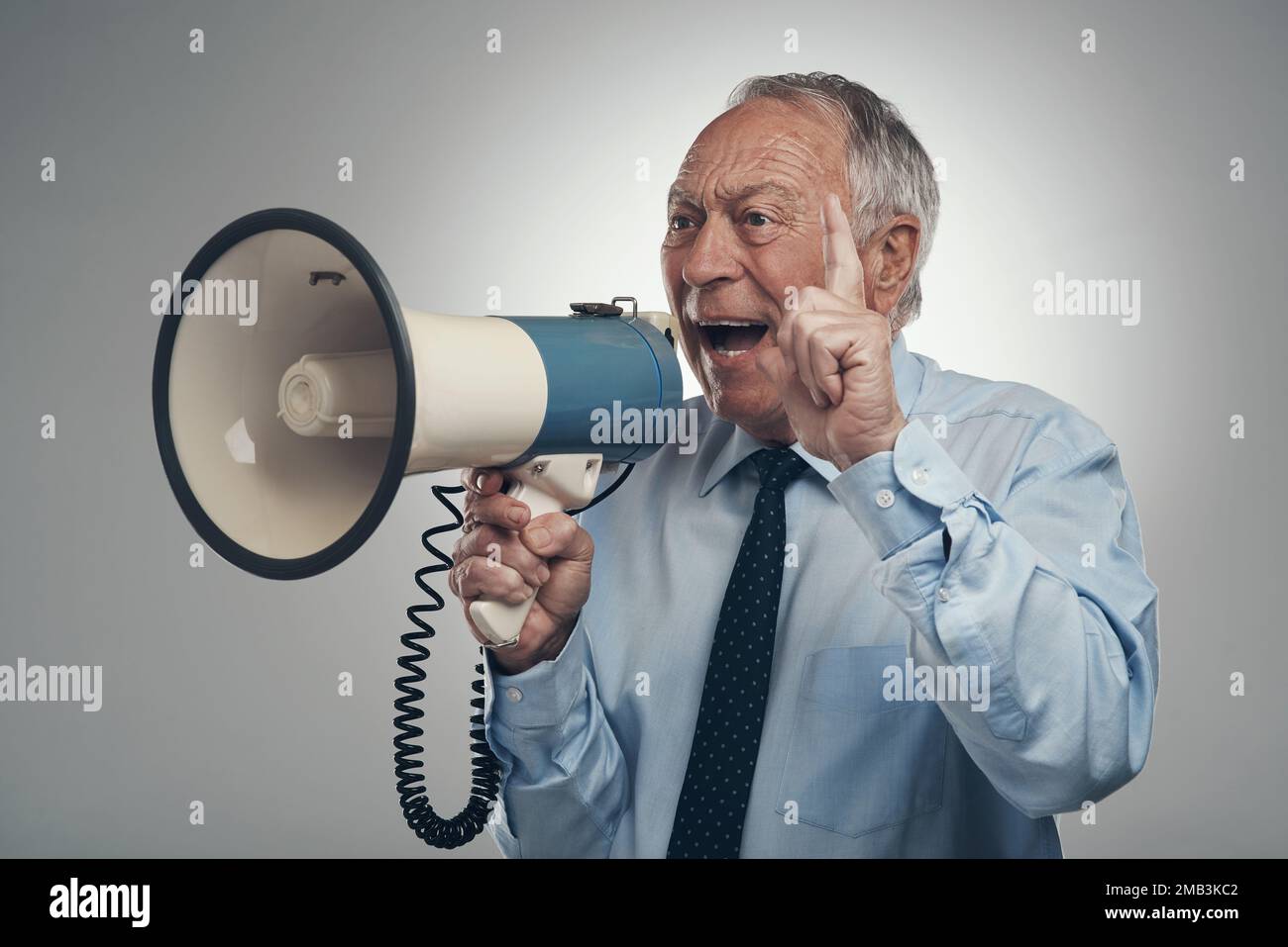 Soutenez la cause. un homme d'affaires senior debout seul sur fond gris dans le studio et utilisant un mégaphone. Banque D'Images