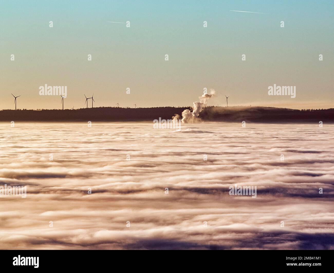 Trois colonnes de vapeur s'élevant de la couverture nuageuse, éoliennes, centrale éolienne à l'horizon, soleil du soir, Koeterberg, Luegde, Weserbergland Banque D'Images