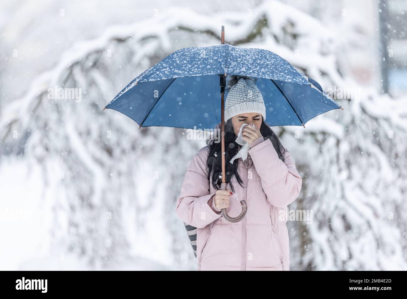 Une femme se dégage de son nez de course debout dans la rue sous un parapluie par temps neigeux. Banque D'Images