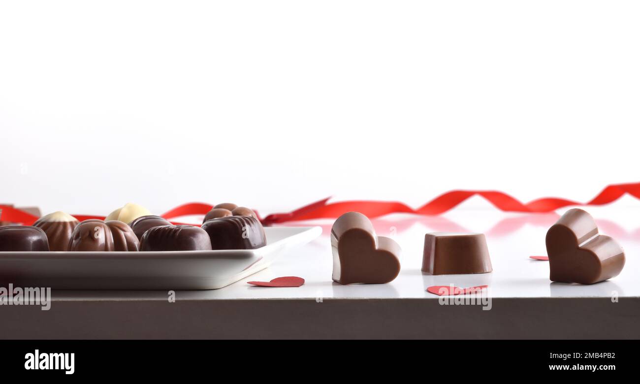 Assortiment de chocolats servi sur une assiette sur une table blanche avec plusieurs chocolats en forme de coeur et un fond blanc isolé. Vue avant. Banque D'Images