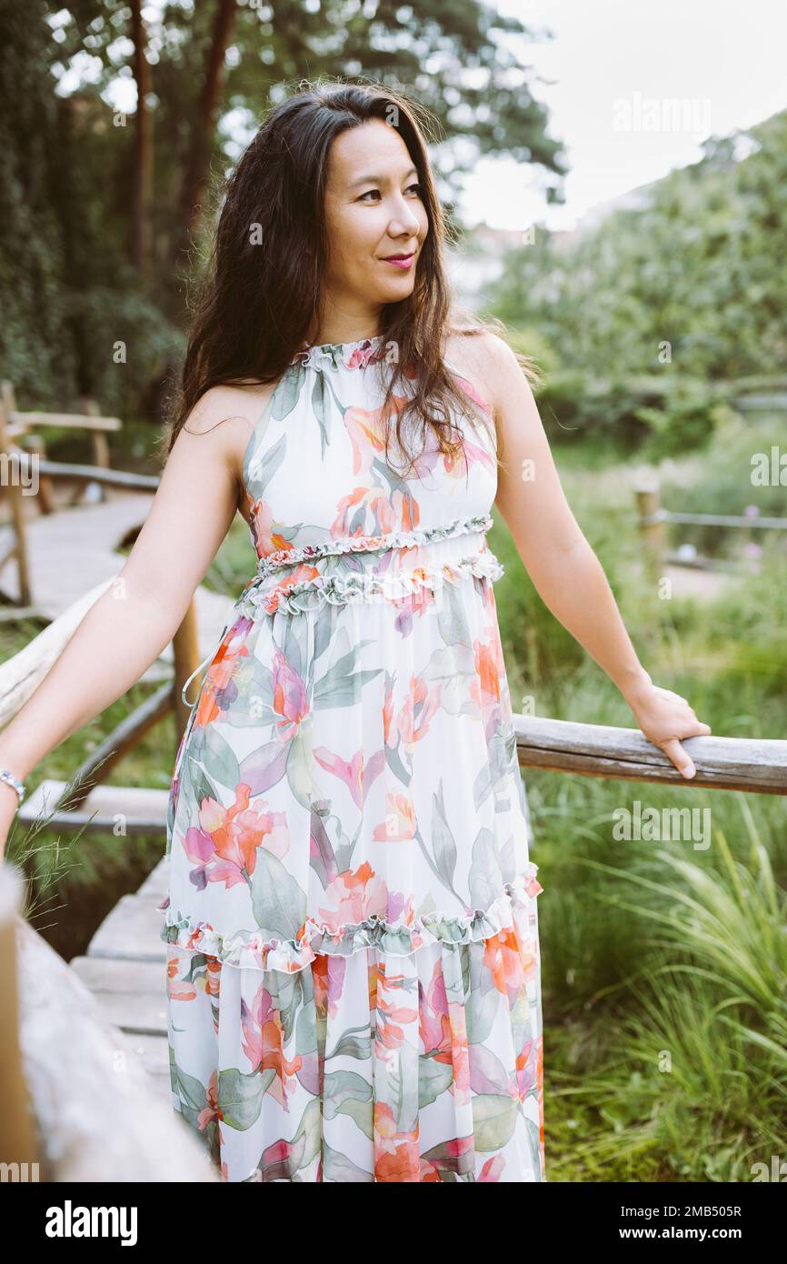 Belle femme japonaise multiraciale heureuse en robe maxi fleurie romantique dans le parc, souriant. Portrait en extérieur. Lumière du soleil, espace de copie Banque D'Images