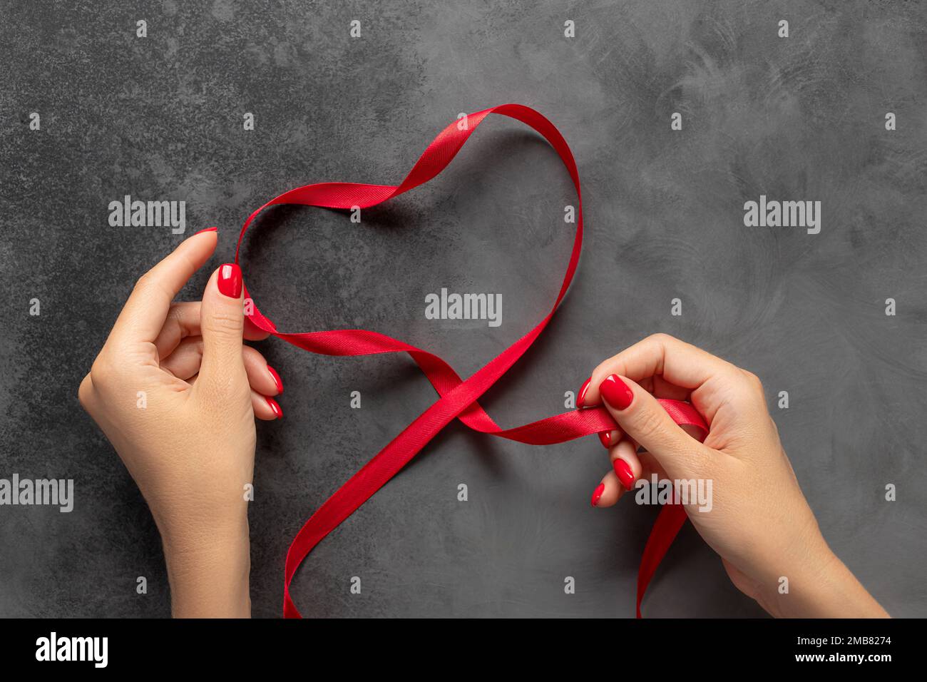 Femme avec beau motif de clou rouge faisant la forme de coeur avec ruban de satin Banque D'Images