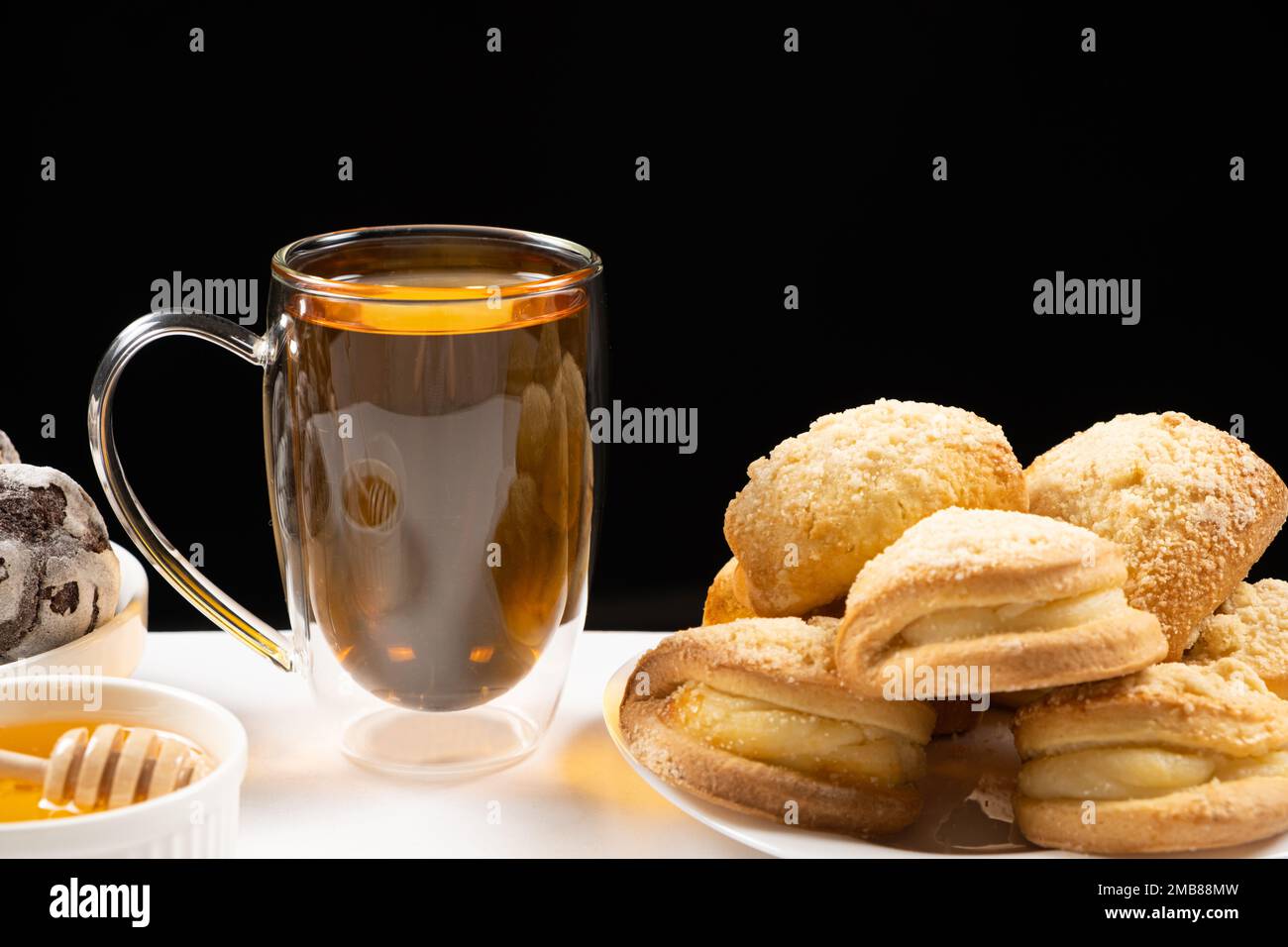 Thé au miel et gâteaux avec garniture crémeuse sur fond noir. Banque D'Images