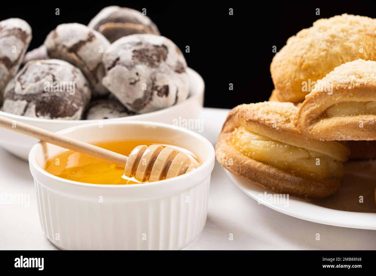 Miel d'abeille naturel liquide dans un bol en céramique blanc avec une cuillère en bois, avec des biscuits au miel et des biscuits au cacao. Banque D'Images