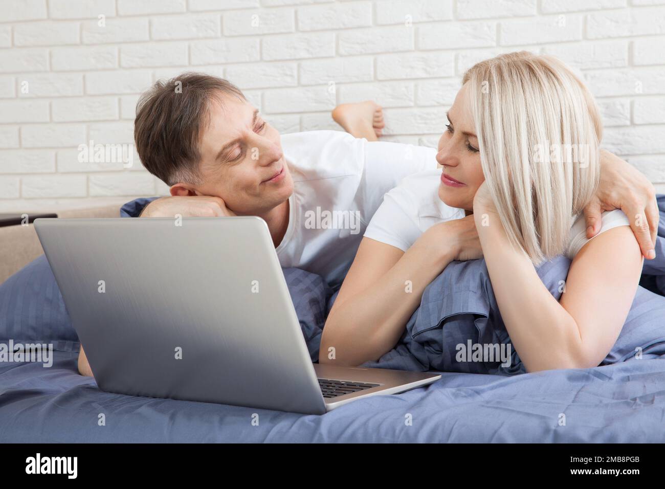 Couple mignon se reposant sur le lit en utilisant un ordinateur portable à la maison dans la chambre Banque D'Images