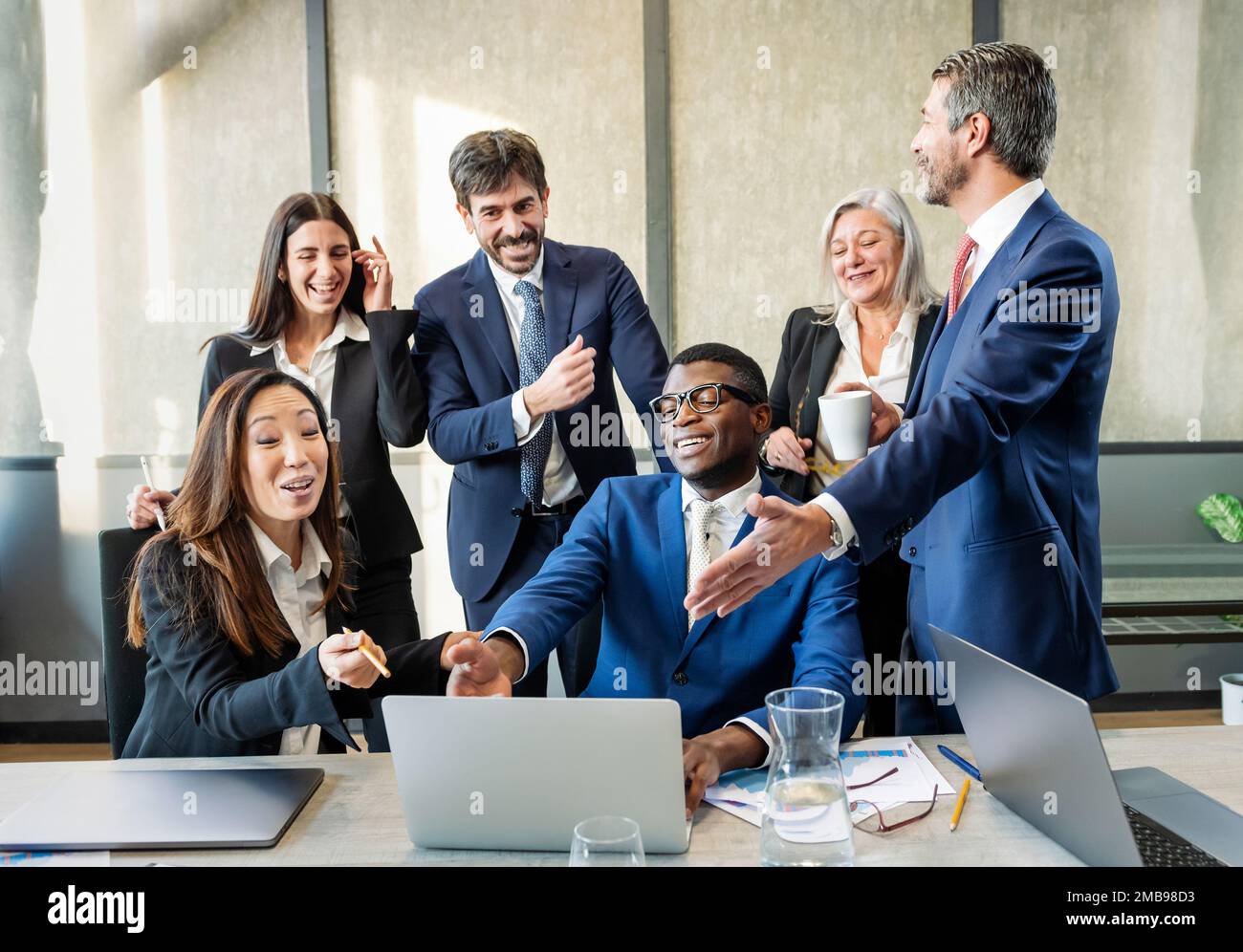 Équipe de collègues masculins et féminins multiraciaux heureux dans des vêtements formels se rassemblant près d'un ordinateur portable et appréciant les nouvelles dans un bureau moderne Banque D'Images