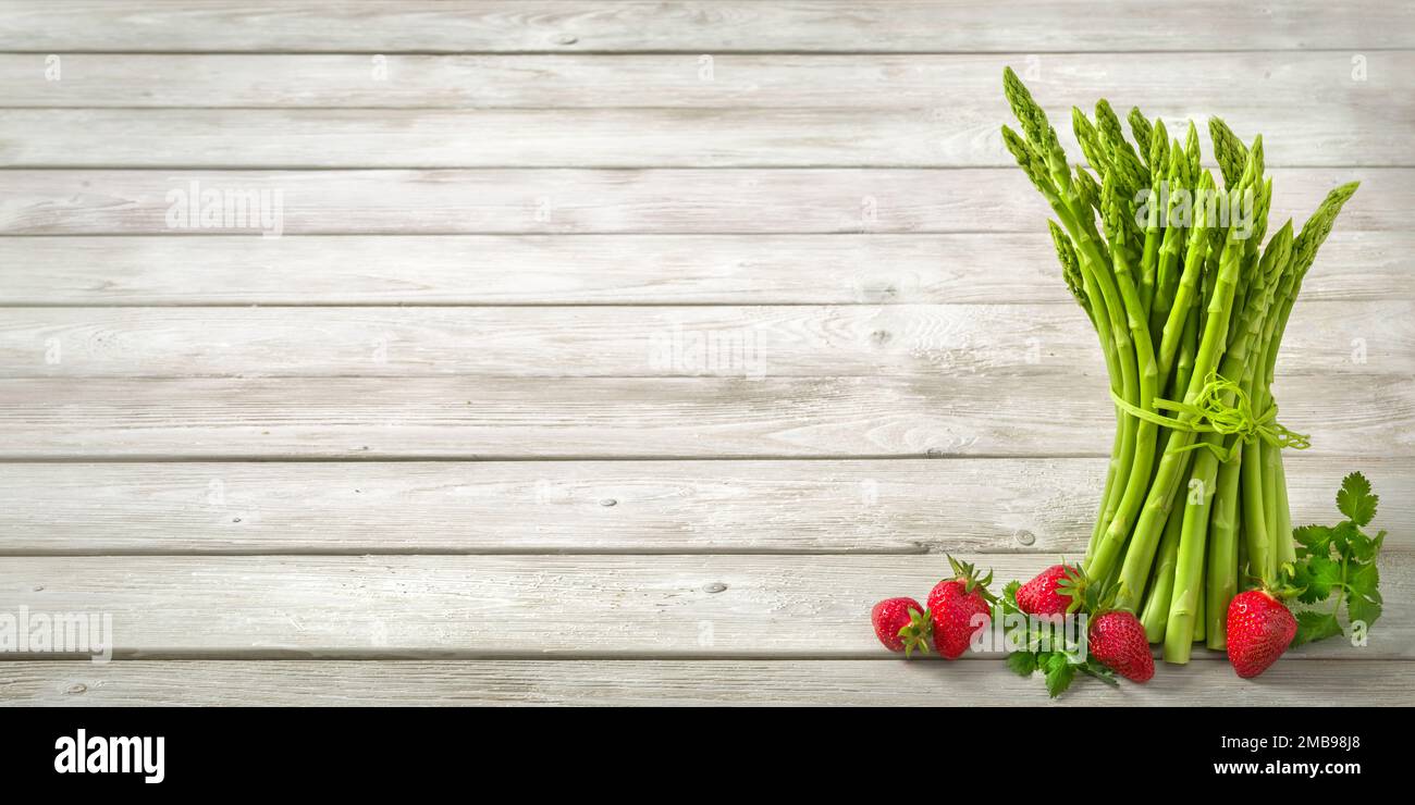 Bouquet d'asperges vertes crues décorées de fraises fraîches sur fond de bois clair et large comme espace de copie Banque D'Images
