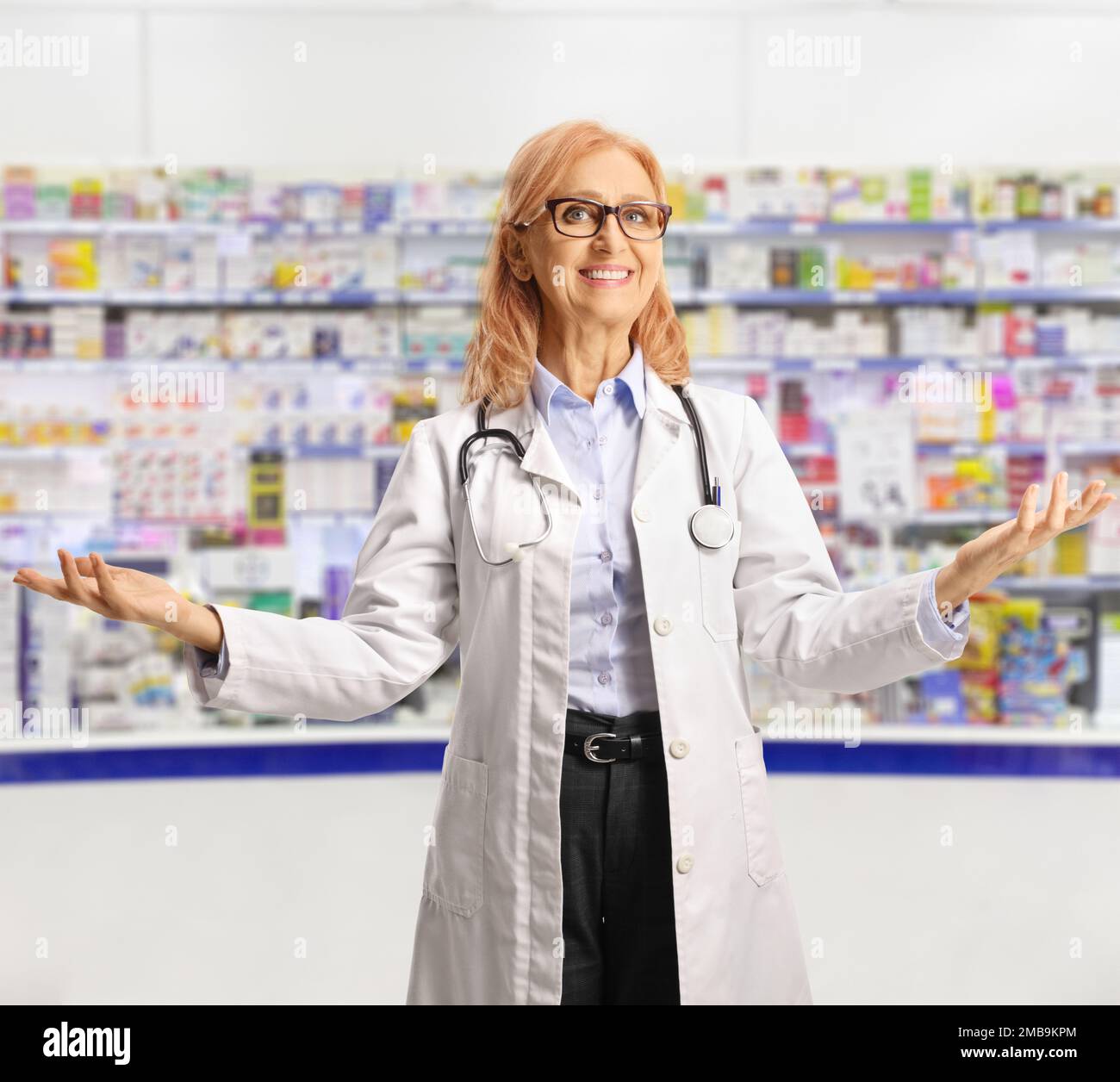 Femme chimiste souriant et gestant avec les mains à l'intérieur d'une pharmacie Banque D'Images