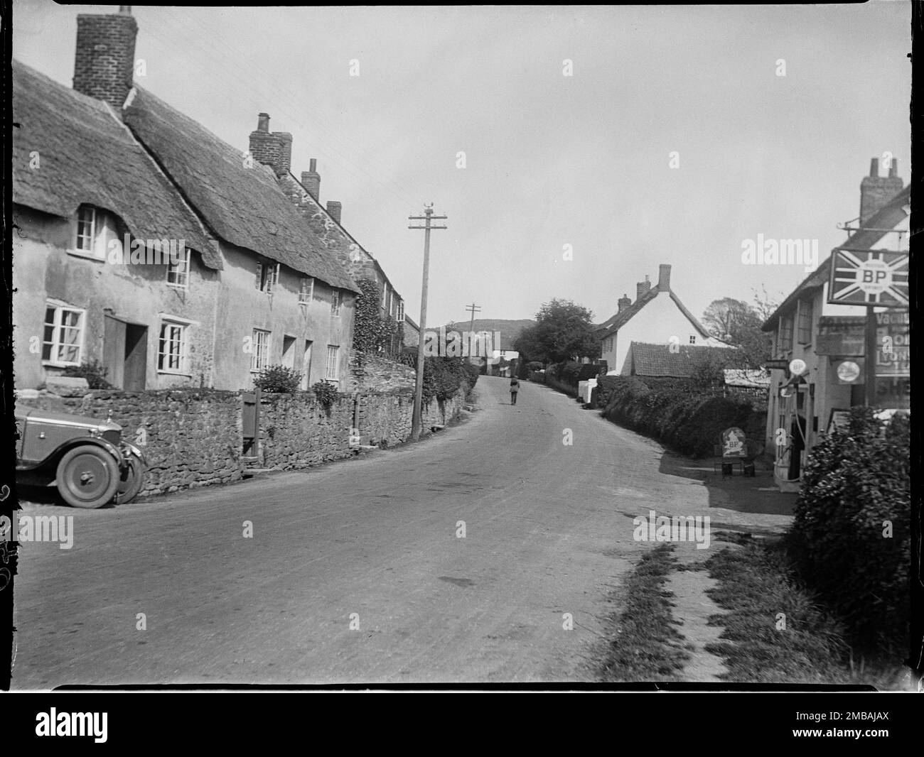 Main Street, Chideock, West Dorset, Dorset, 1925. En regardant vers l'est le long de main Street, après Apple Tree Cottage et Apple Tree thatch, et de l'autre côté de la route, une boutique avec une pompe à essence et panneau BP dehors. Banque D'Images