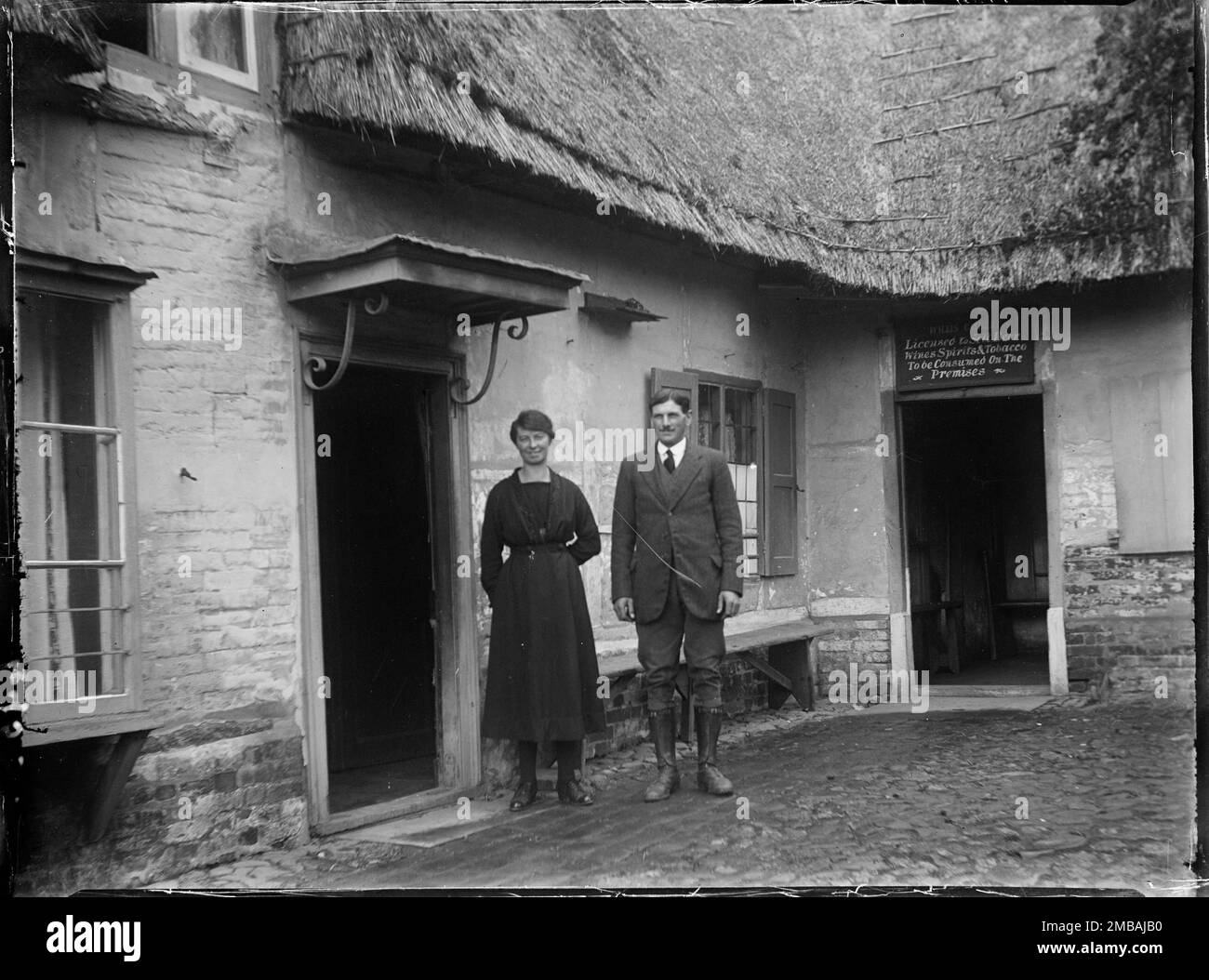 Royal Oak Inn, Wootton Rivers, Wiltshire, 1923. Un portrait de M. &amp; Mme Gilbert debout dans la cour du Royal Oak Inn. Un panneau au-dessus de l'une des portes indique que Willis Gilbert était autorisé à vendre de la bière, des vins, des spiritueux et du tabac, qui seront consommés sur place. Banque D'Images