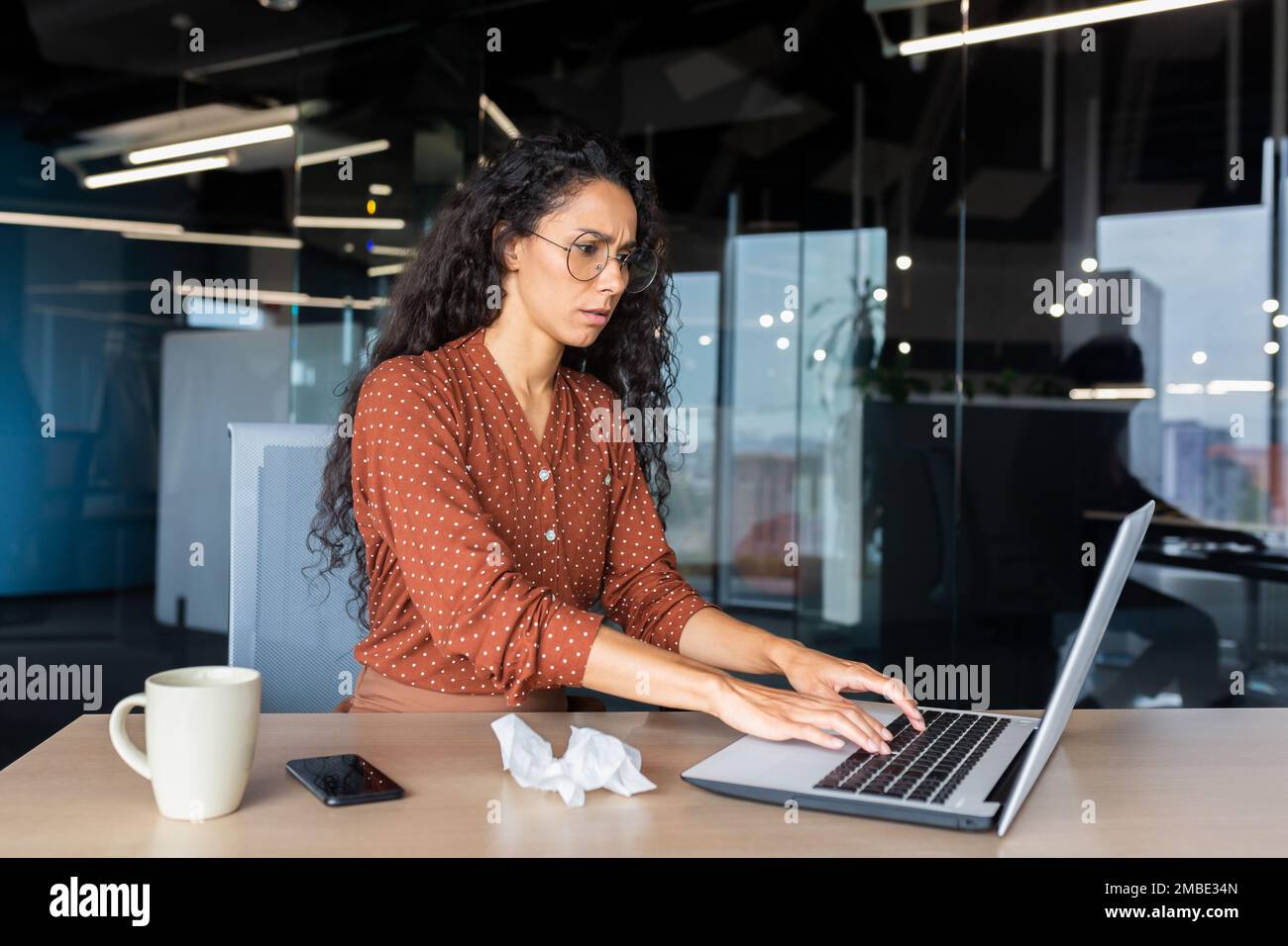 Jeune femme américaine fatiguée travaillant sur un ordinateur portable au bureau. Elle est tombée malade, elle ne se sent pas bien, les heures supplémentaires. Banque D'Images