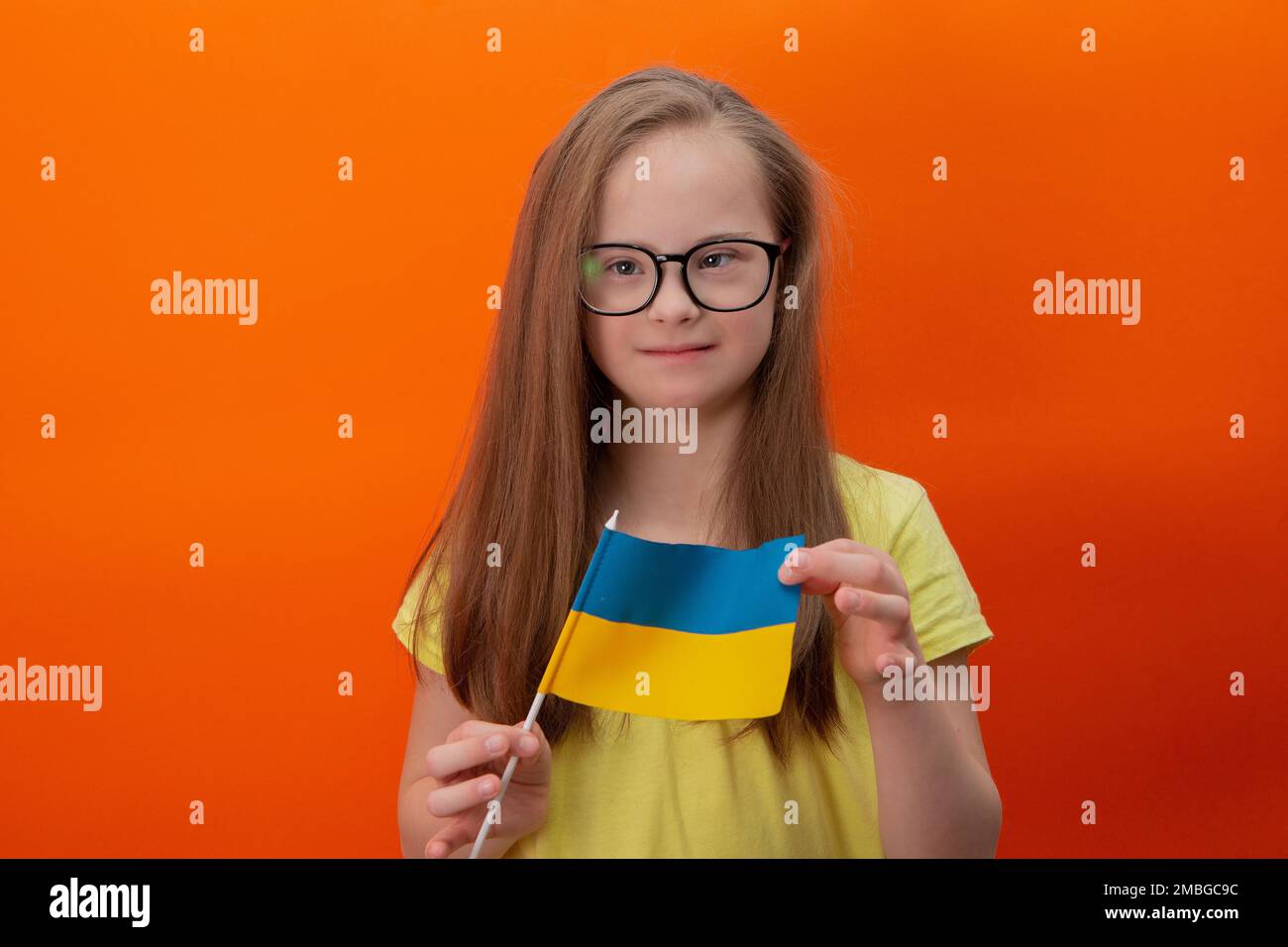 Une fille avec le syndrome de Down tient le drapeau de l'Ukraine. arrière-plan orange Banque D'Images