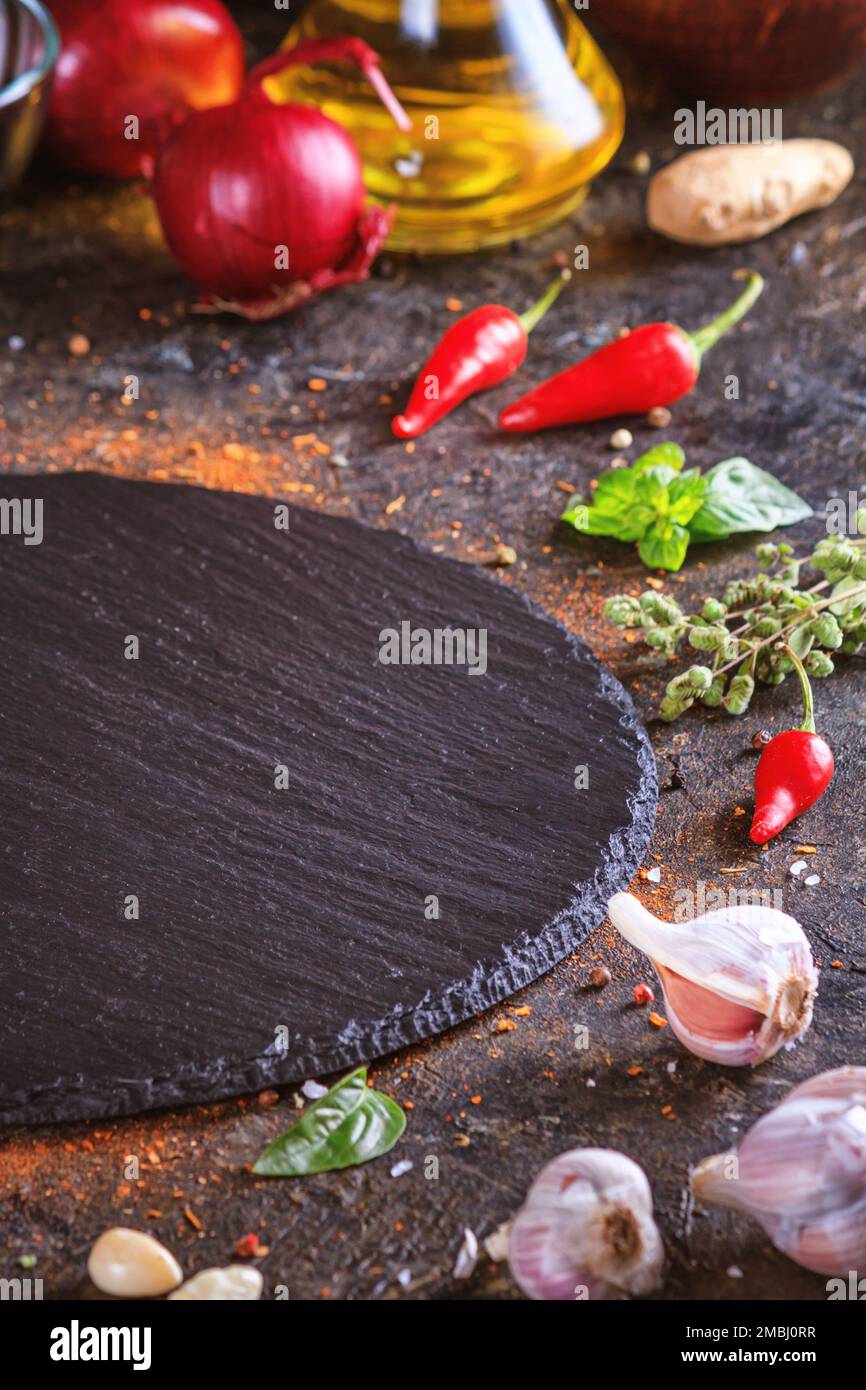 Décor culinaire avec table ronde en ardoise, huile d'olive dans une carafe et légumes.Espace vide pour le menu ou la recette avec mise au point sélective Banque D'Images