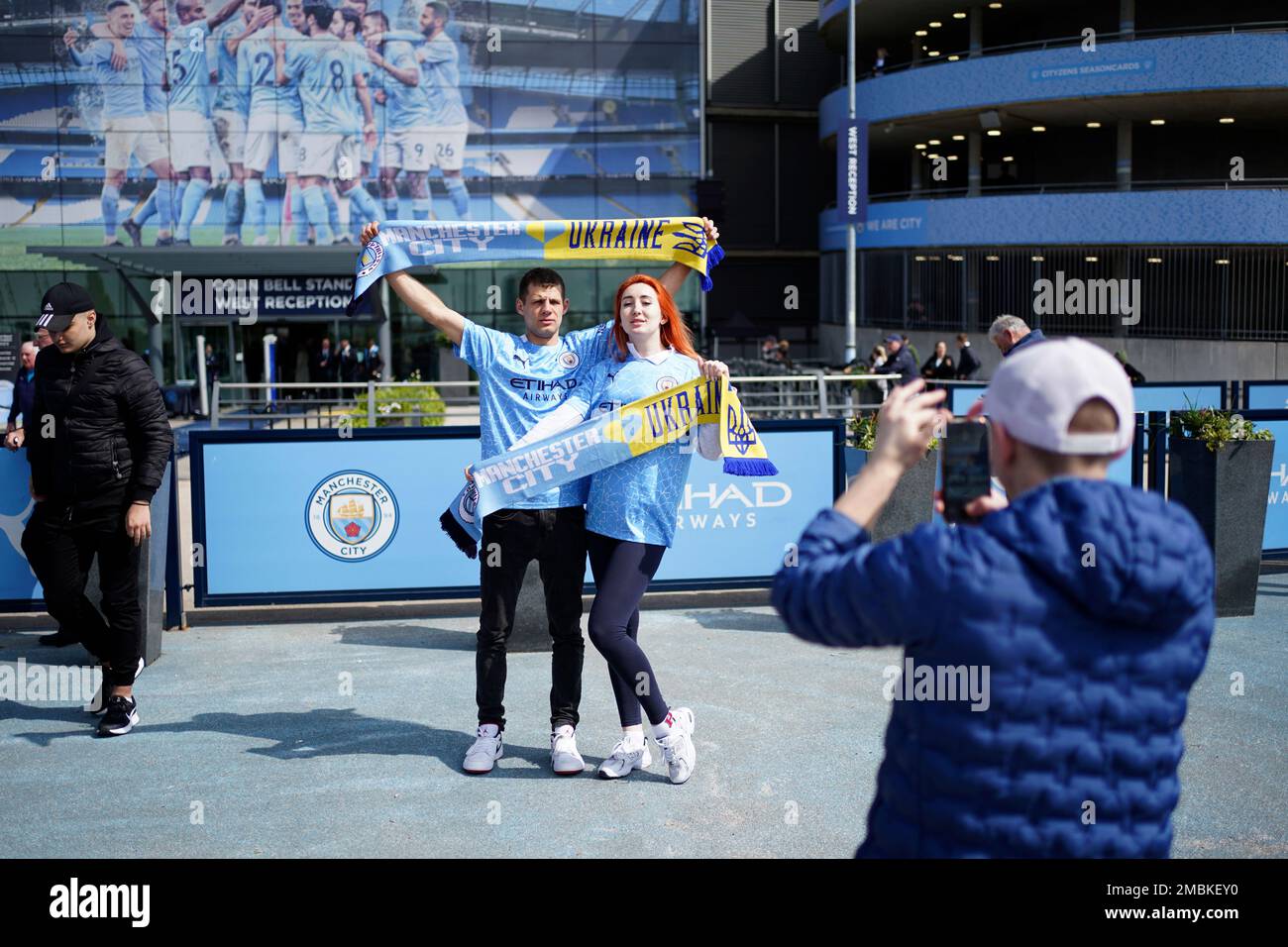 Manchester City fans holding scarfs with the Ukrainian colors pose for photos outside the stadium before the English Premier League soccer match between Manchester City and Watford at Etihad stadium in Manchester, England, Saturday, April 23, 2022. (AP Photo/Jon Super) Banque D'Images