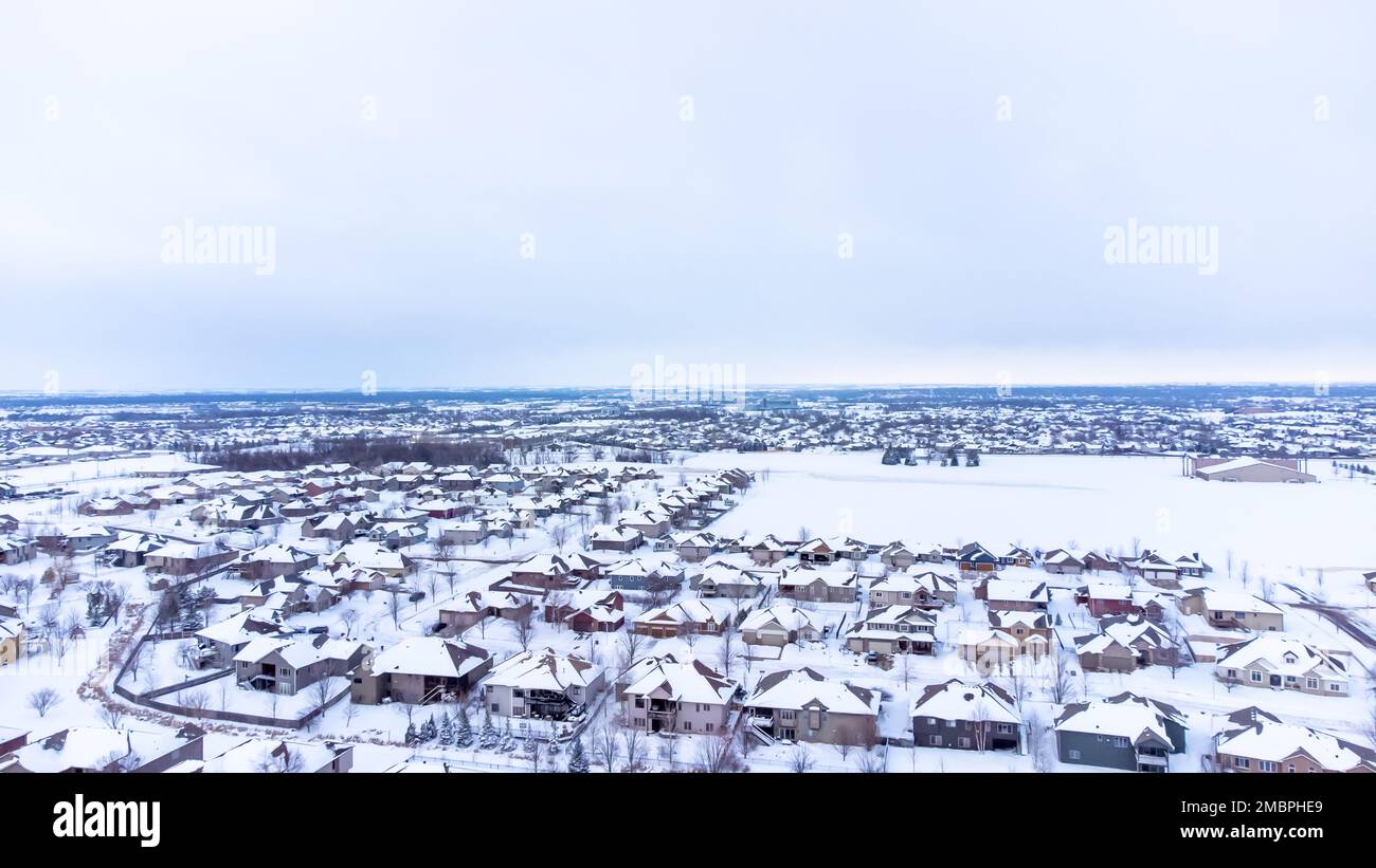 Vue aérienne par drone d'un quartier résidentiel de banlieue enneigé avec des rangées de toits blancs et de maisons. Banque D'Images