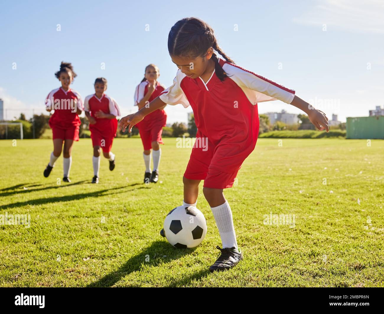 Football, entraînement ou sport et une équipe de filles jouant avec un ballon ensemble sur un terrain de pratique. Fitness, football et herbe avec les enfants en train de courir ou Banque D'Images